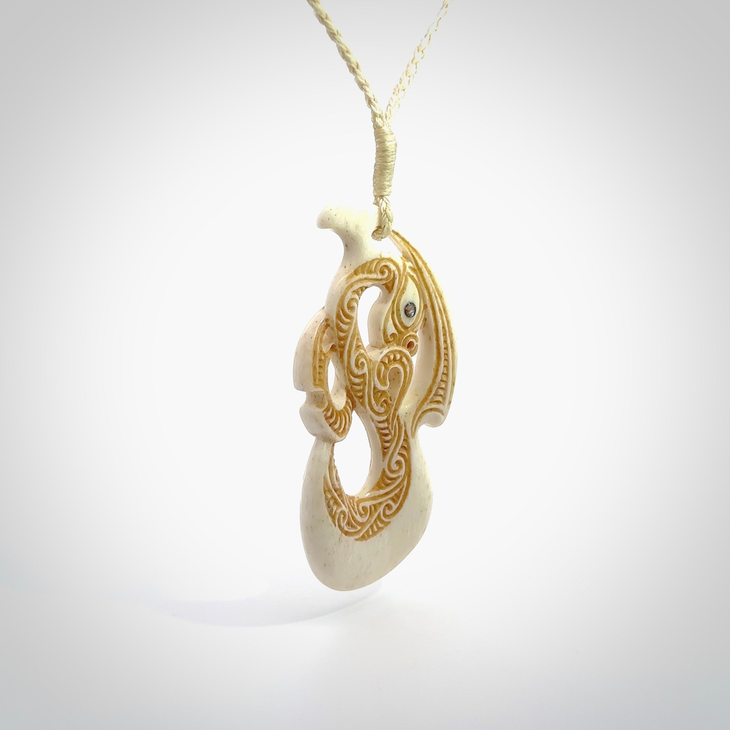 This picture shows a carved manaia in bone. The artist has carved traditional decorative kowhaiwhai designs into the body and these run up the insides of the manaia. These have specific meanings. It is provided with a hand-plaited beige cord that is length adjustable. Free shipping worldwide.