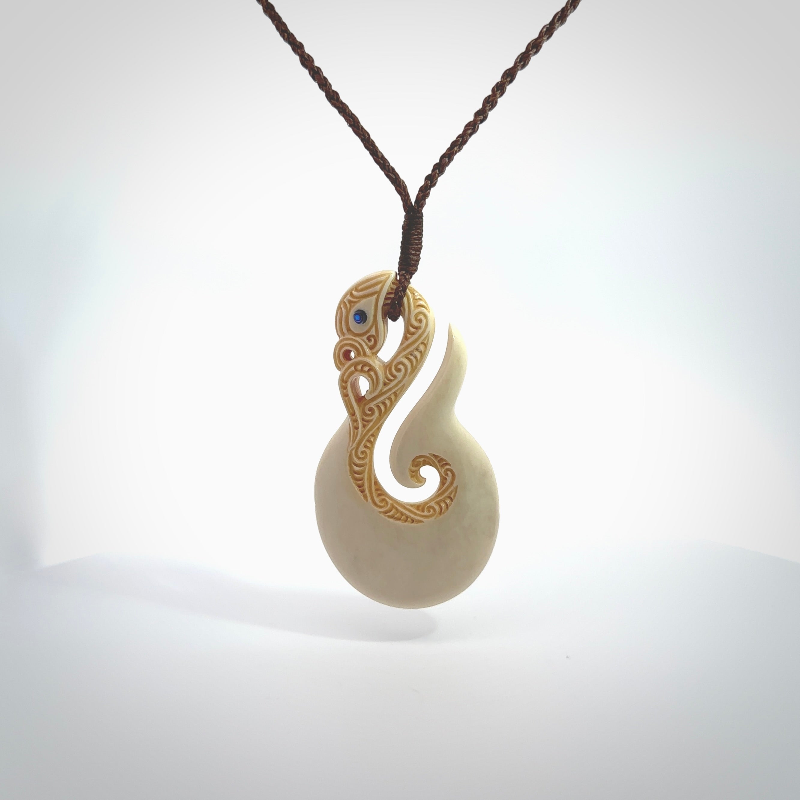 Hand carved bone manaia with matau, hook pendant. Hand made by Andrew opughty, delivered with an adjustable brown cord. Manaia with Paua shell eyes and engraving. One only necklace.