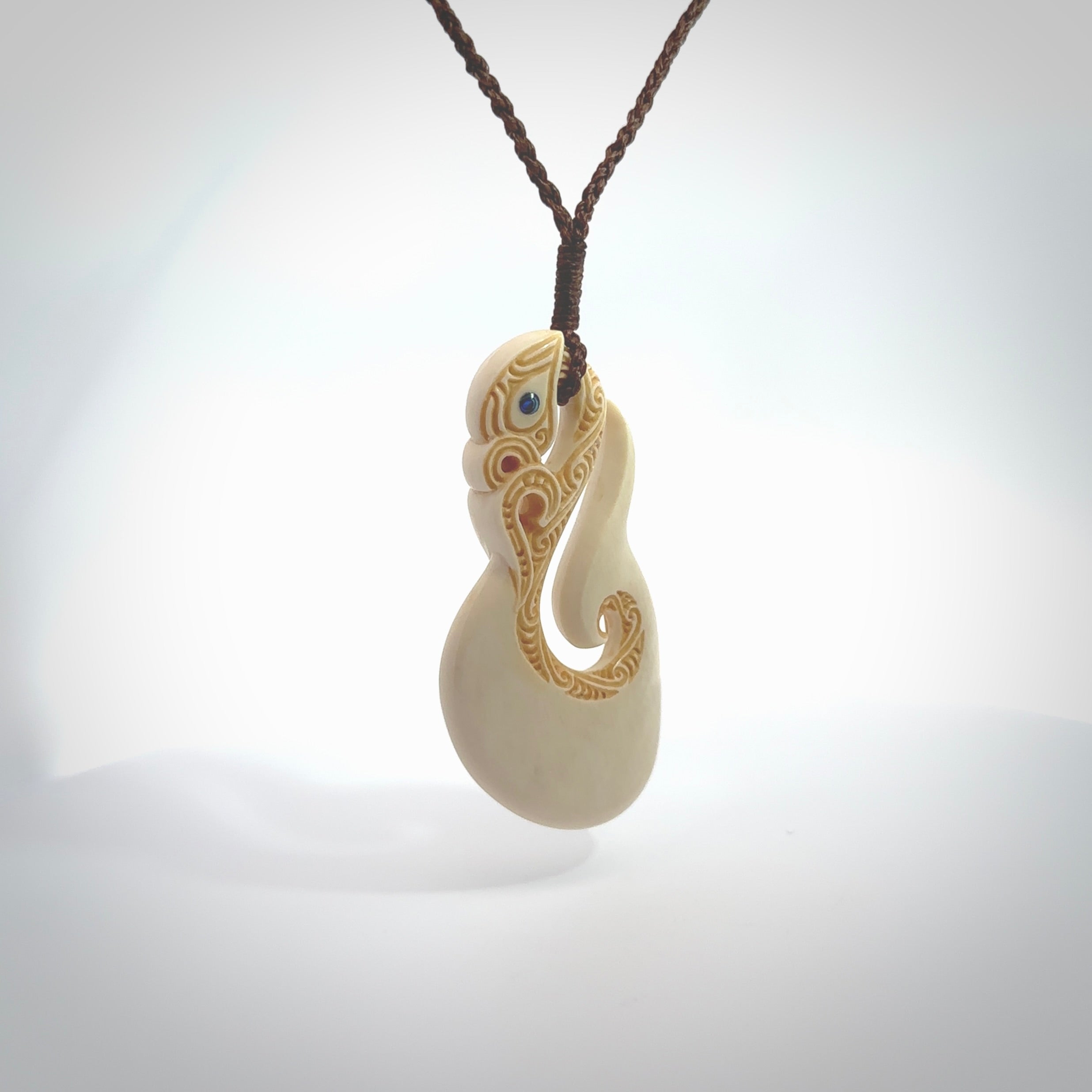 Hand carved bone manaia with matau, hook pendant. Hand made by Andrew opughty, delivered with an adjustable brown cord. Manaia with Paua shell eyes and engraving. One only necklace.