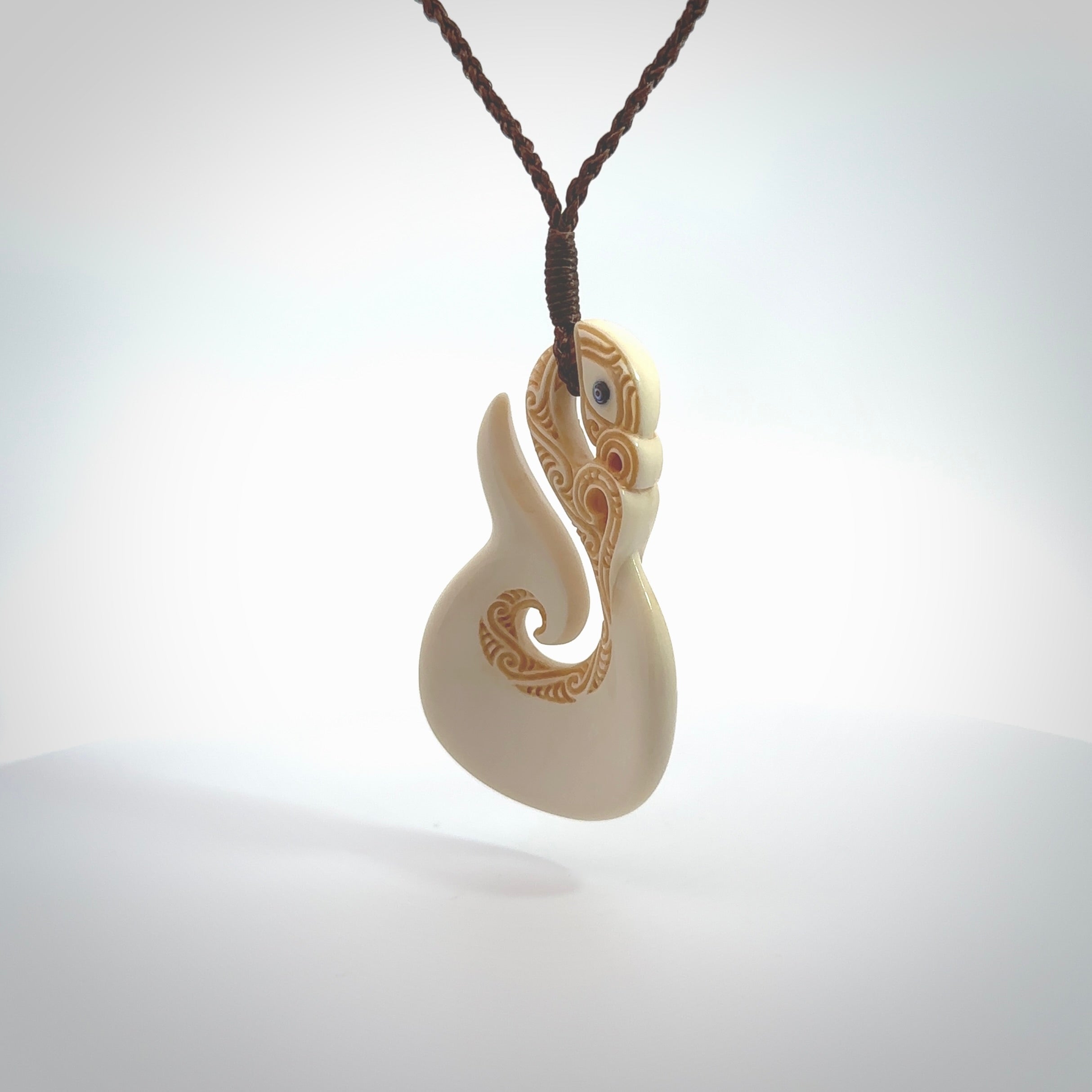 Hand carved bone manaia with matau, hook pendant. Hand made by Andrew opughty, delivered with an adjustable brown cord. Manaia with Paua shell eyes and engraving. One only necklace.