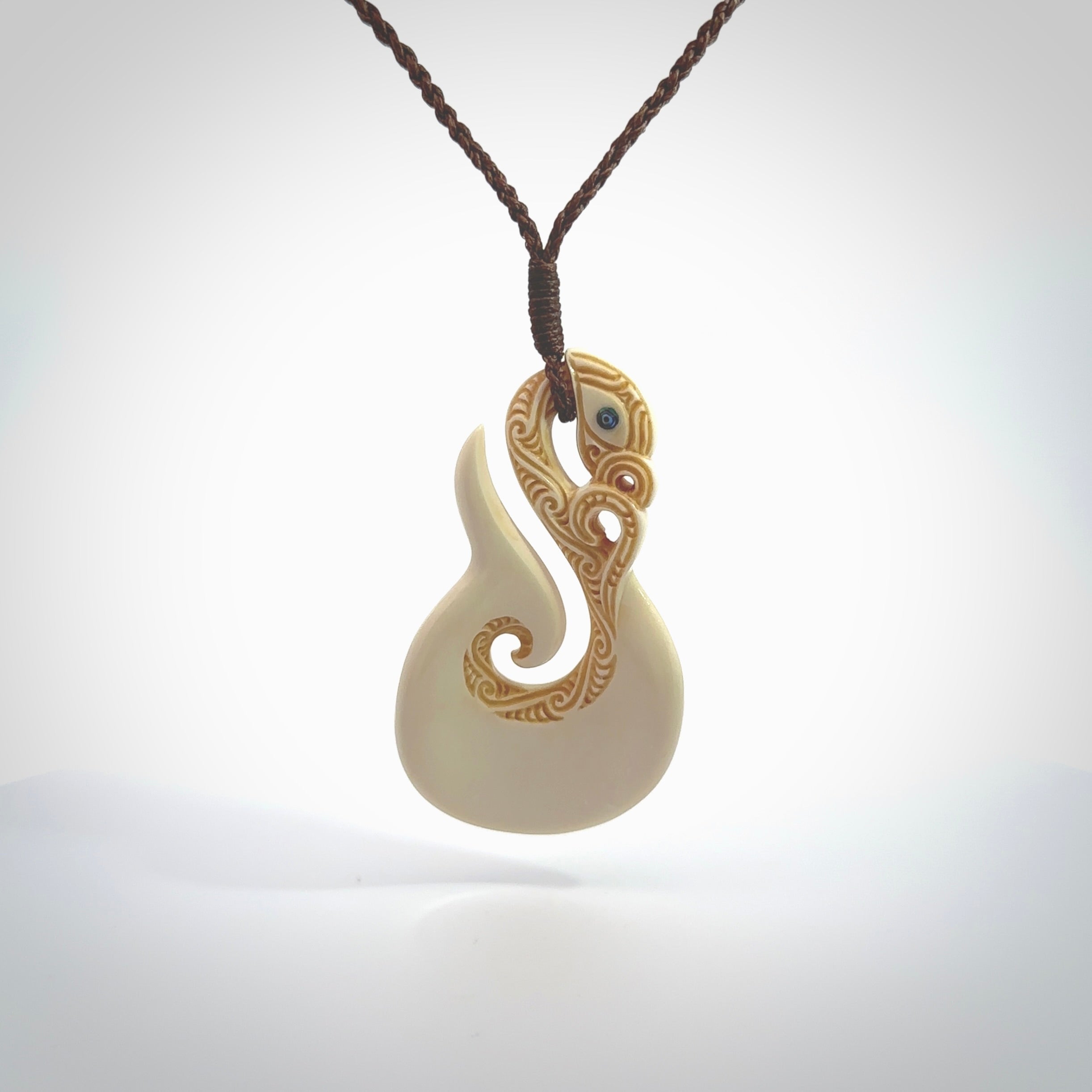 Hand carved bone manaia with matau, hook pendant. Hand made by Andrew opughty, delivered with an adjustable brown cord. Manaia with Paua shell eyes and engraving. One only necklace.