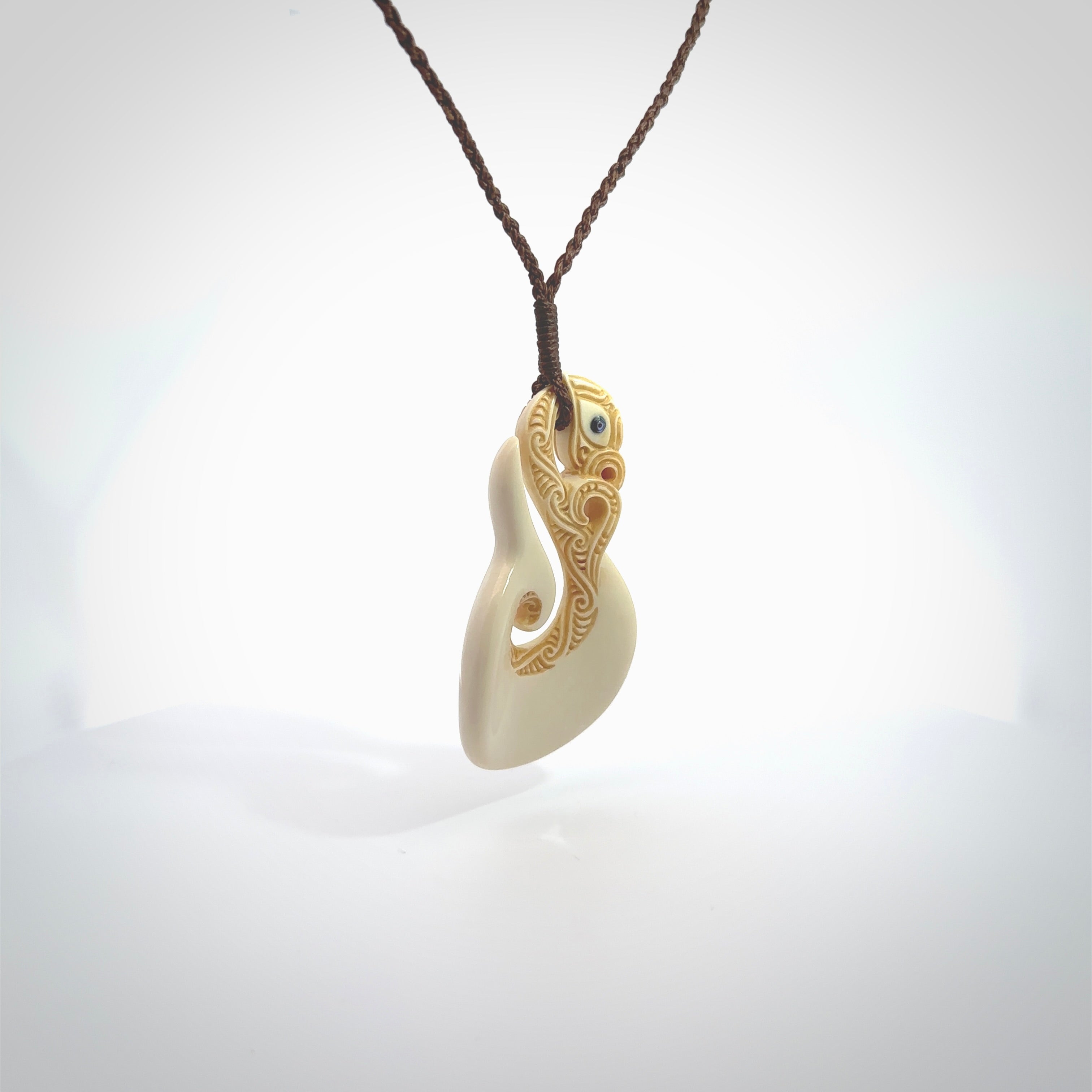 Hand carved bone manaia with matau, hook pendant. Hand made by Andrew opughty, delivered with an adjustable brown cord. Manaia with Paua shell eyes and engraving. One only necklace.