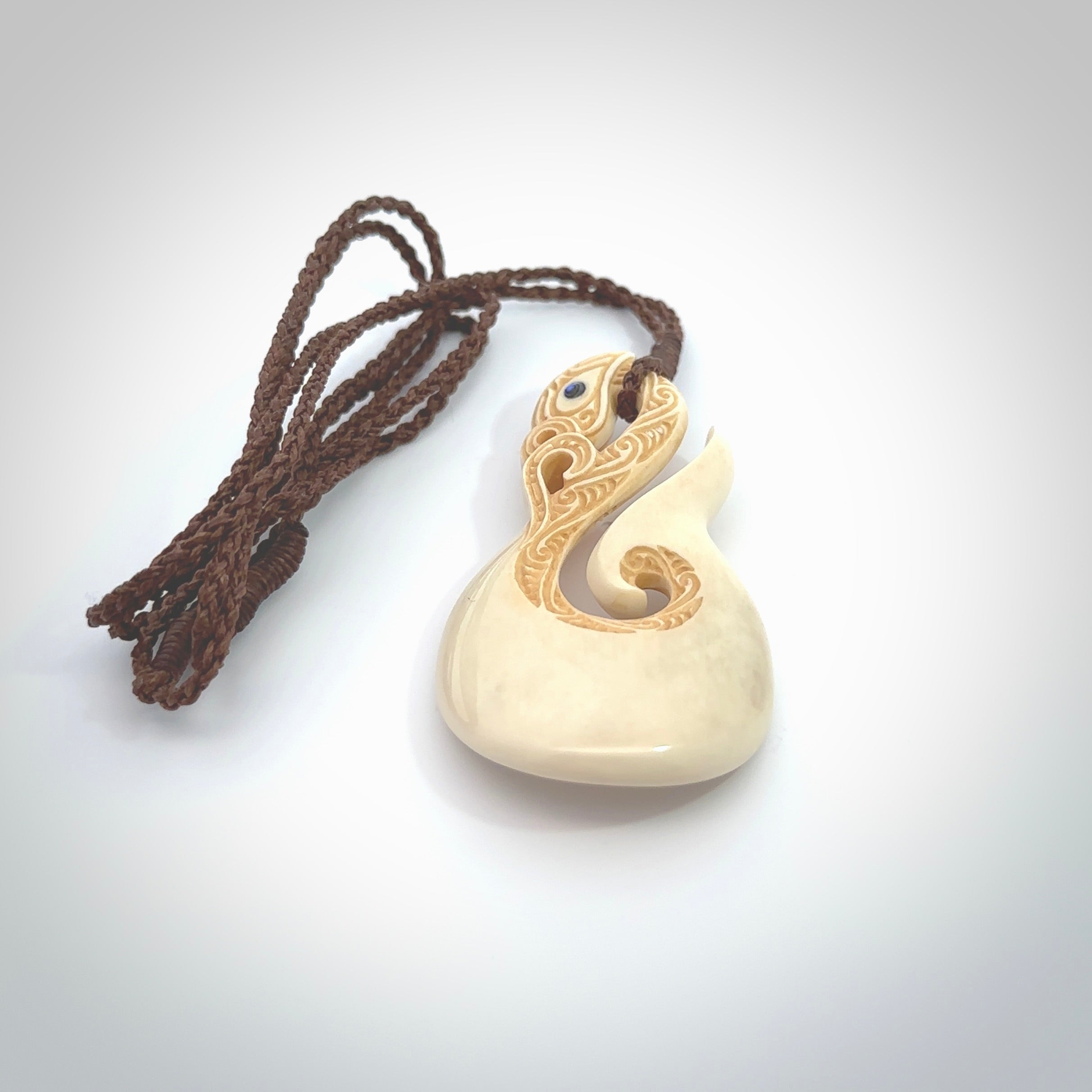 Hand carved bone manaia with matau, hook pendant. Hand made by Andrew opughty, delivered with an adjustable brown cord. Manaia with Paua shell eyes and engraving. One only necklace.