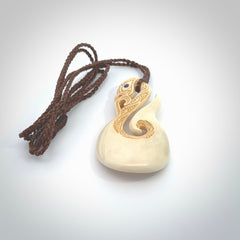 Hand carved bone manaia with matau, hook pendant. Hand made by Andrew opughty, delivered with an adjustable brown cord. Manaia with Paua shell eyes and engraving. One only necklace.