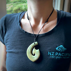 This picture shows a carved Matau, Hook, in New Zealand Jade. It is a hook shaped pendant pendant that culminates in a fish tail. It is provided with a black coloured cord that is length adjustable. Hand made in New Zealand by Andrew Doughty.