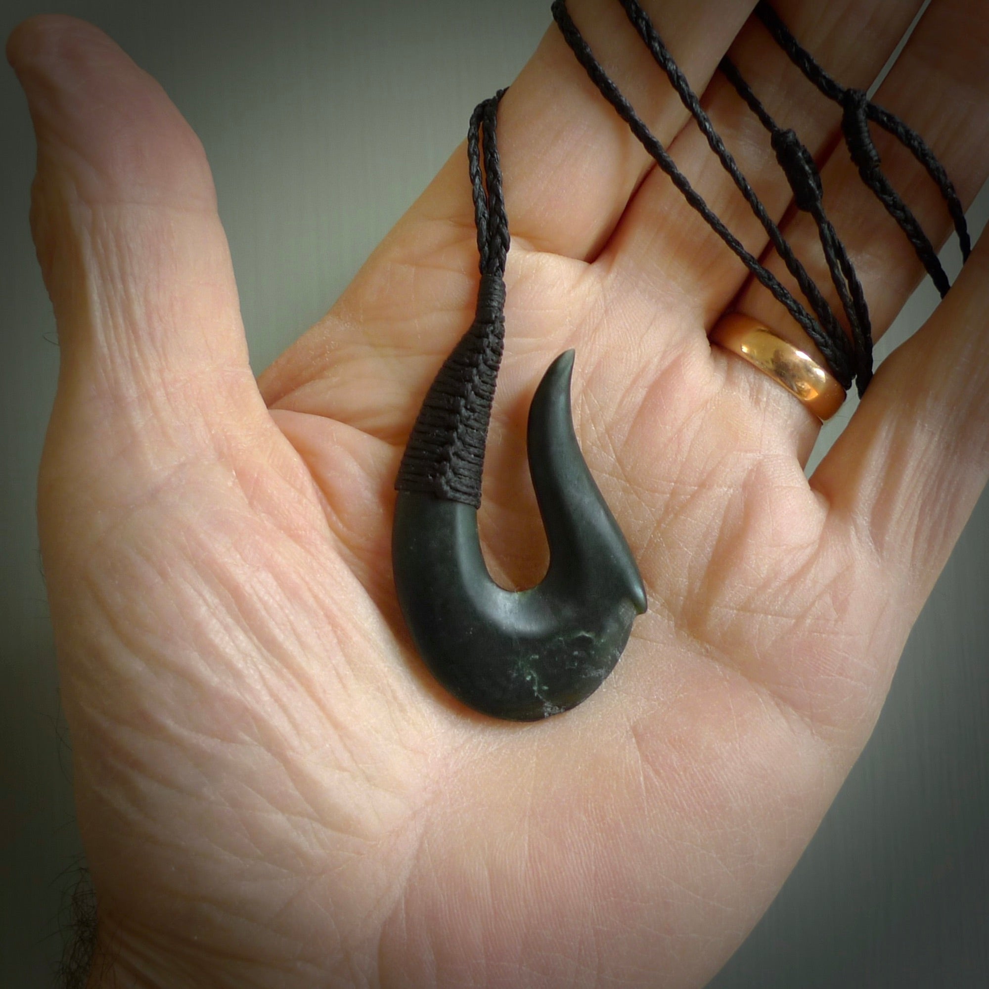 This photo shows a greenstone hook, or matau, pendant. It is a beautiful deep green jade. The cord is plaited olive green and the length can be adjusted.