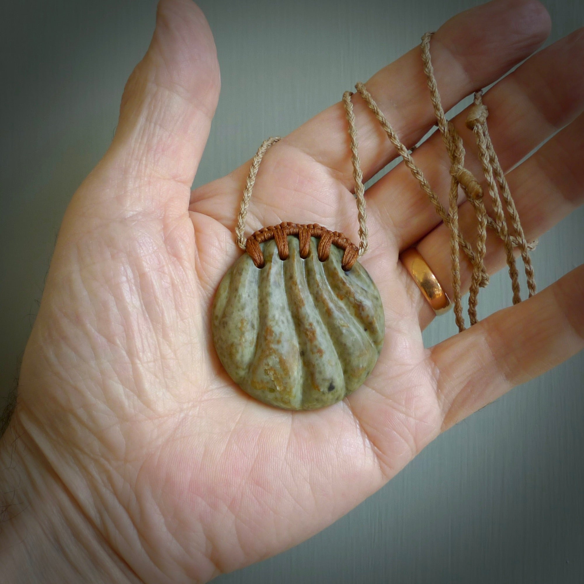 This picture shows a hand carved sea shell disc pendant made from a flowering green/orange coloured flower jade. Hand made by Ana Krakosky. It is provided with an adjustable 4-Plait Kalahari tan cord and chestnut brown binding. Delivered to you with Express Courier.