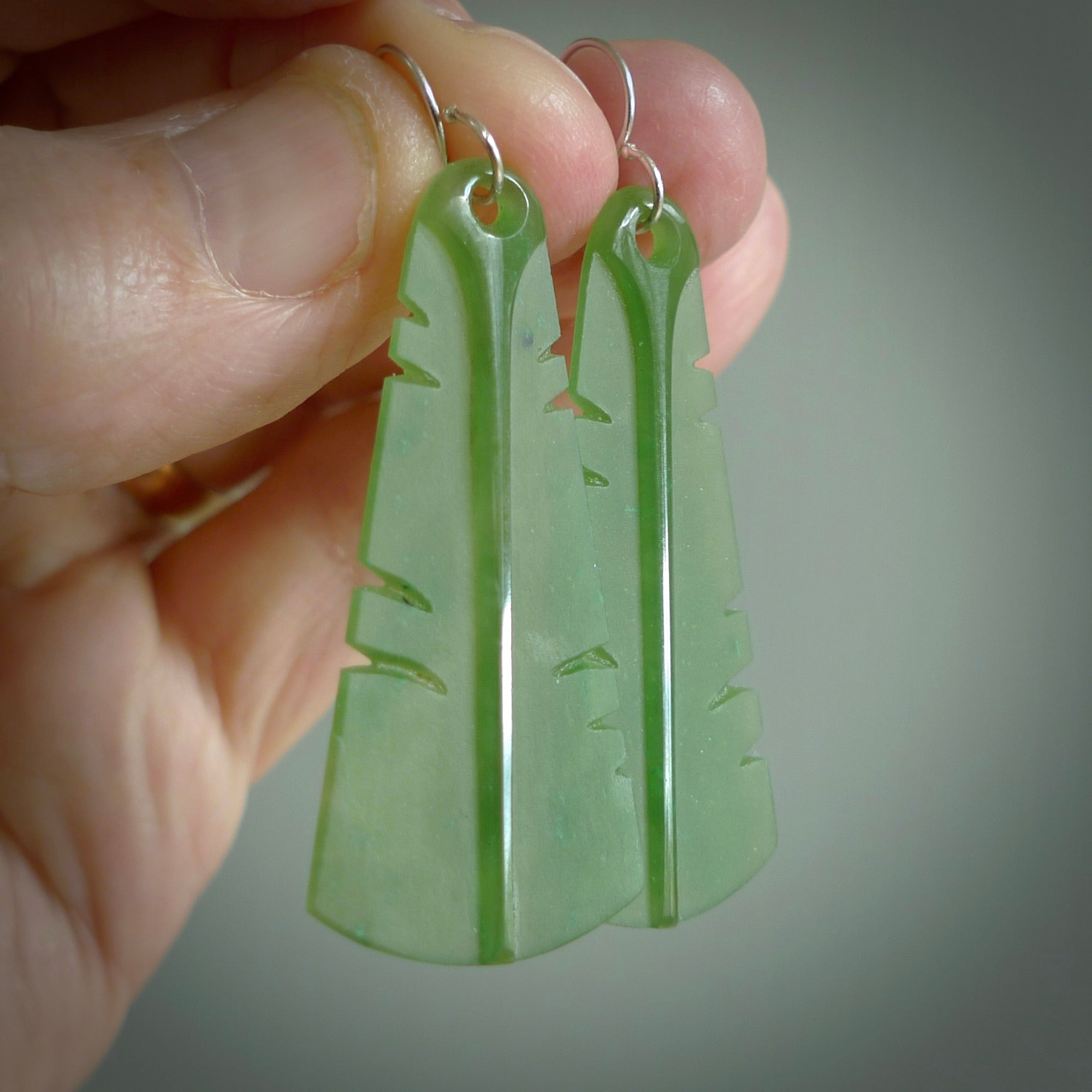 This picture shows New Zealand Pounamu, jade feather earrings with sterling silver hooks. Hand made unique and contemporary feather earrings by Kerry Thompson. Hand carved here in New Zealand from New Zealand Jade. One pair only.