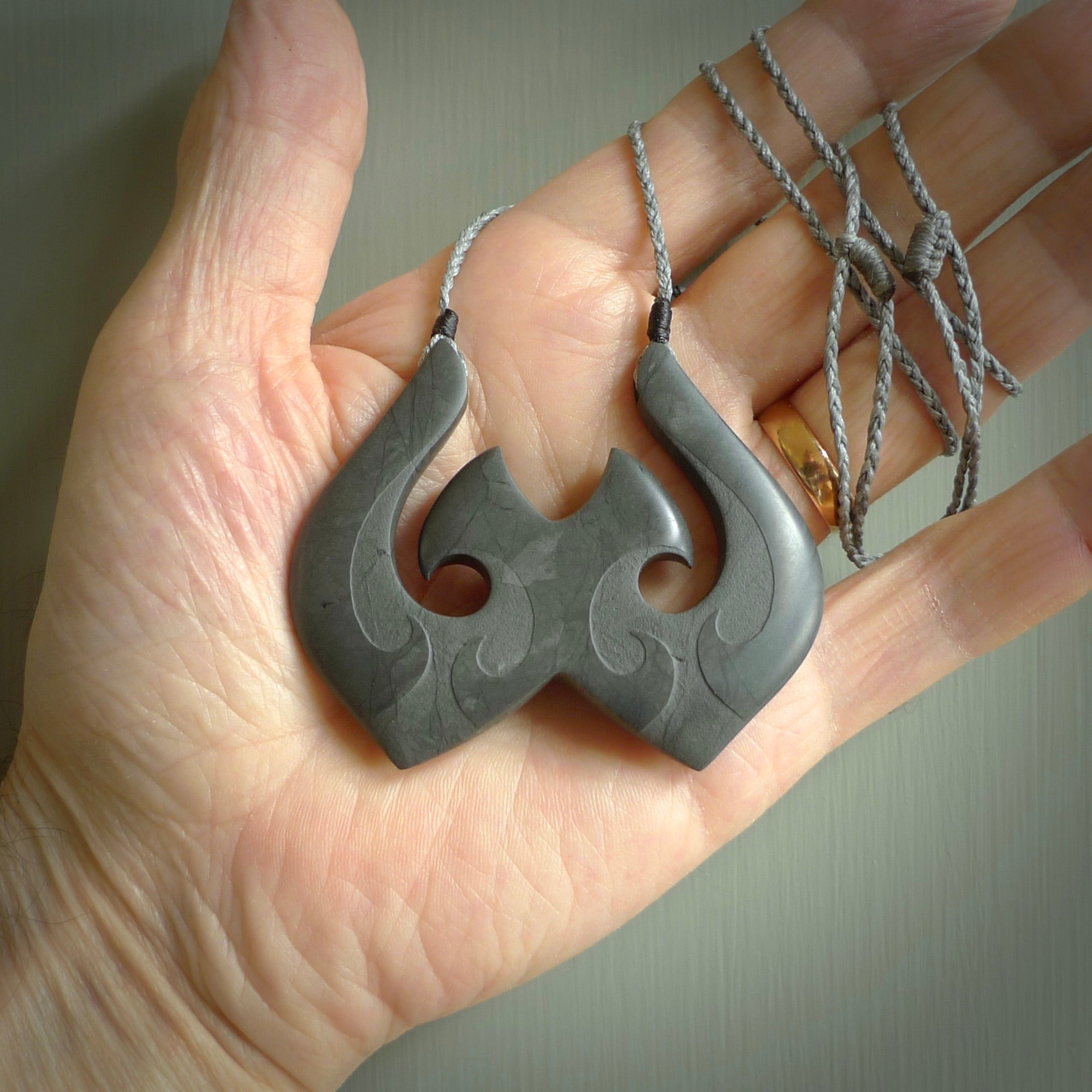 A hand carved large New Zealand Argillite double Hook, Matau, necklace. The cord is a grey colour and is adjustable in length. A large sized hand made double hook necklace by New Zealand artist Rueben Tipene. One off work of art to wear.