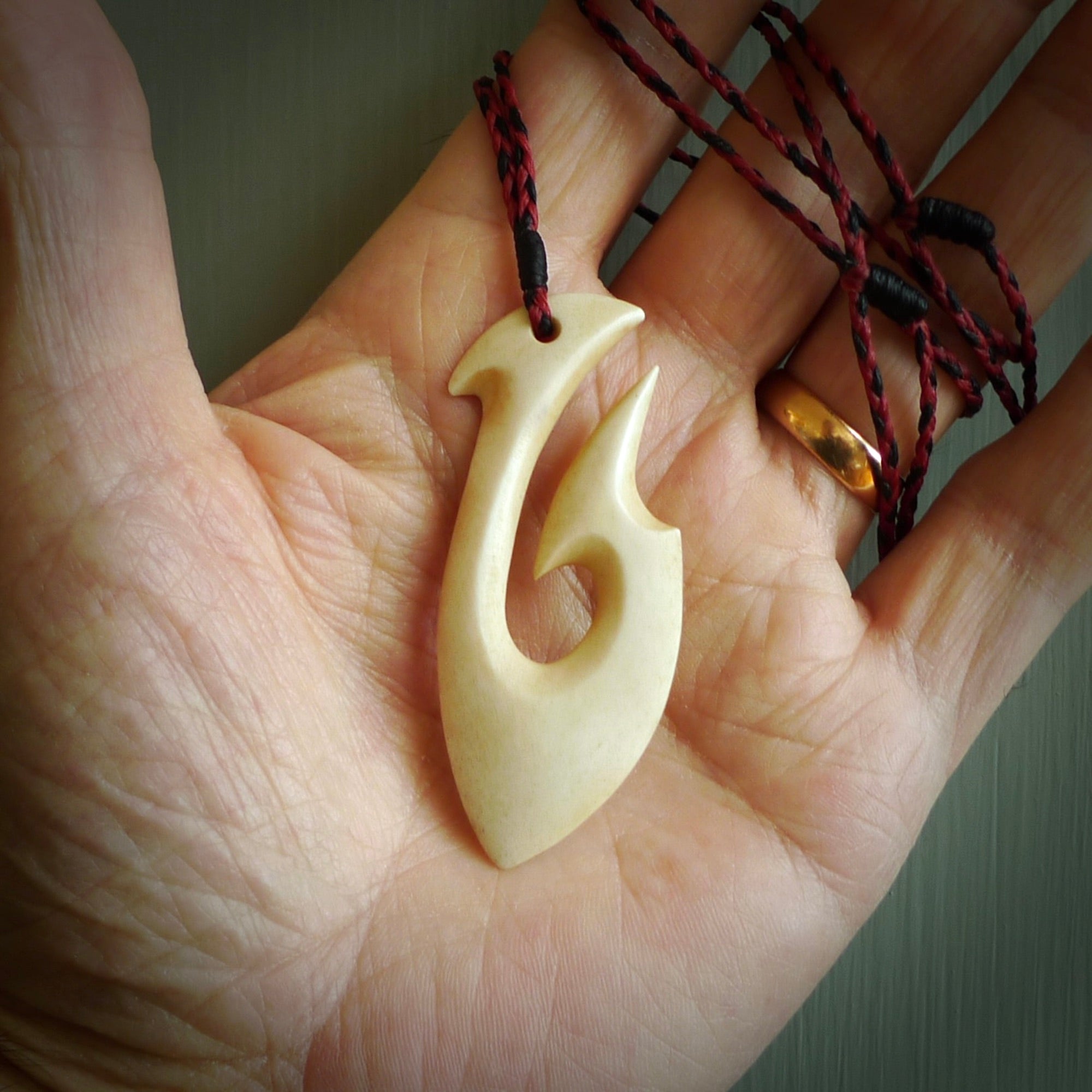 This is a larger bone hook, or matau, pendant carved from a piece of bone. The cord is a black and red colour and the length of the cord can be adjusted. It is a large sized pendant and is well carved. A beautiful piece of traditional jewellery.