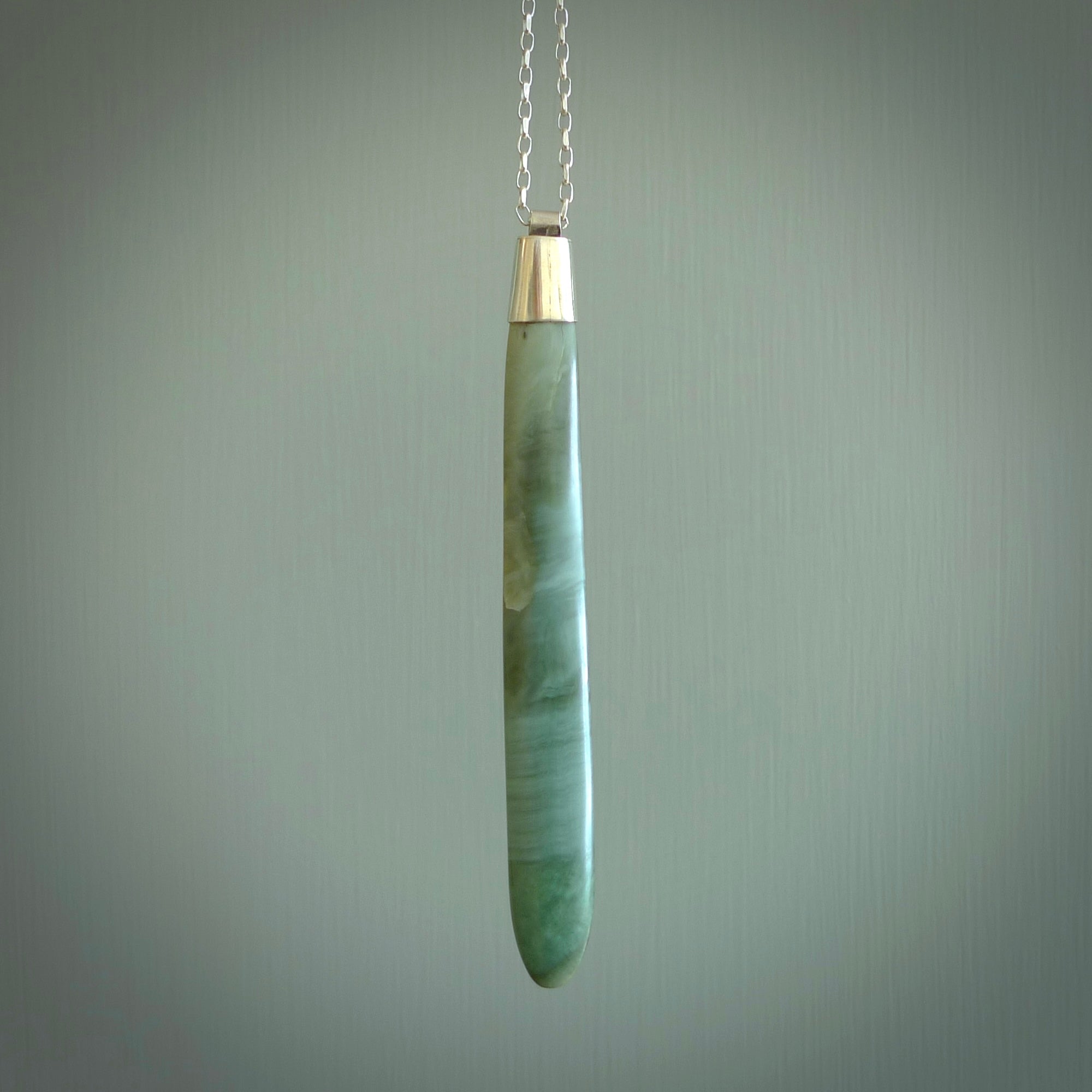 This picture shows a hand carved Inanga Pounamu, jade drop pendant with sterling silver cap and chain. The jade is a very dark green with a shimmer of light blue tones in the stone. It is suspended from a sterling silver clasp and we supply a sterling silver chain. Delivery is free worldwide.