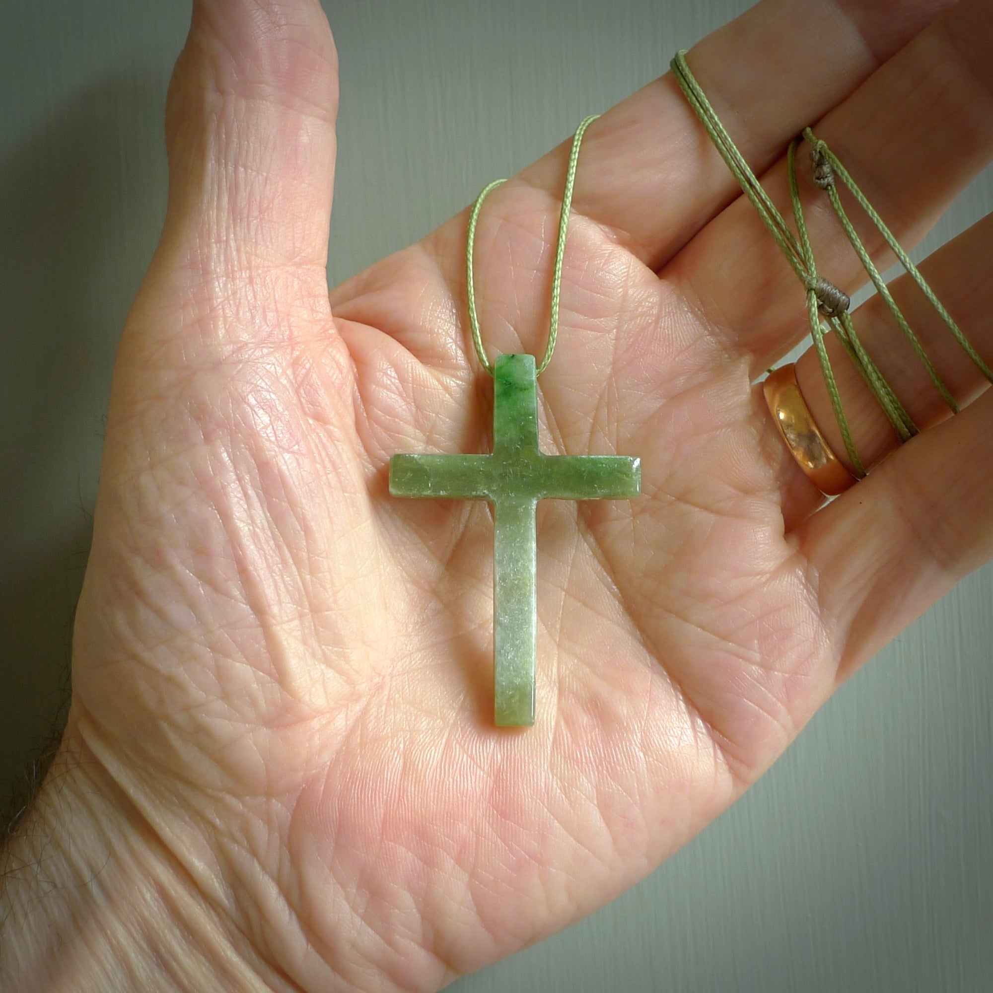 Hand carved jade cross. Made from New Zealand jade. Christian cross for sale online.This picture shows a green jade cross suspended on a fine, plaited cord. The cross is hand carved jade cross. Made from New Zealand jade. Christian cross for sale online.