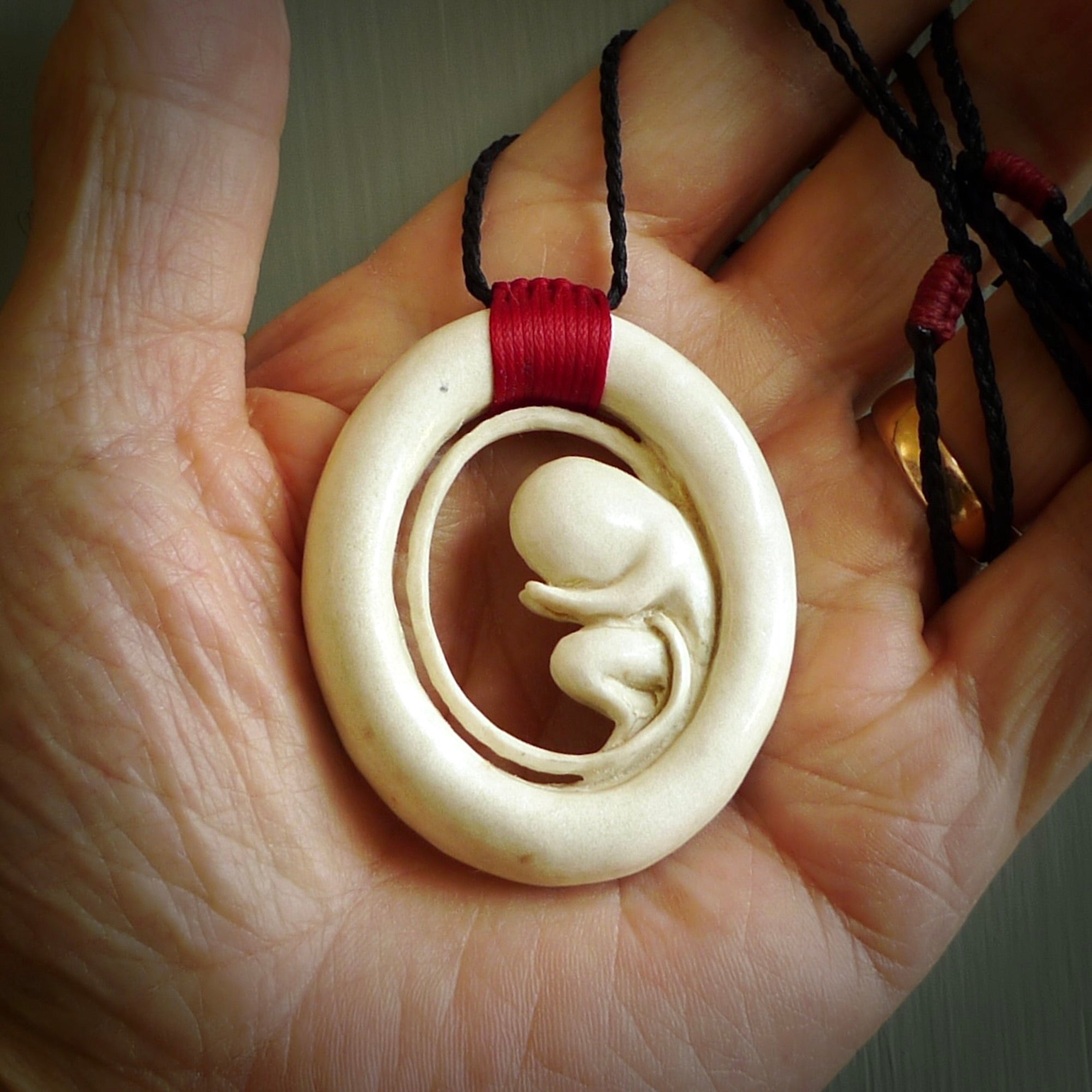 Hand carved deer antler fetus pendant. Hand carved by NZ Pacific. Free postage worldwide. Hand made fetus necklace from deer antler. Fetus necklace for men and women. Delivered with adjustable black cord with Red binding.