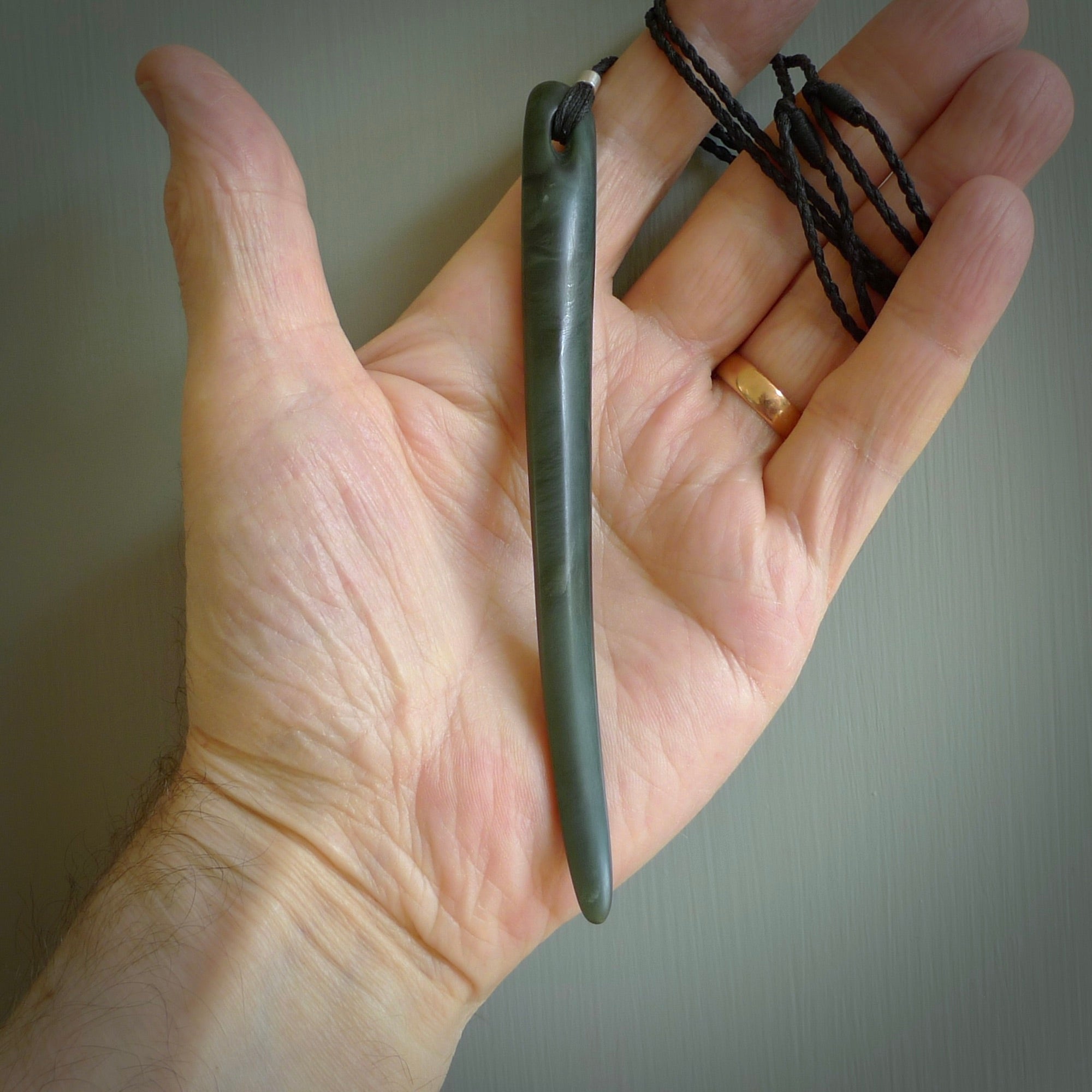 This picture shows a hand carved Pounamu jade beak drop pendant with adjustable cord. The jade is a very dark green with shimmering blue tones in the stone. It is suspended from a adjustable cord. Delivery is free worldwide.