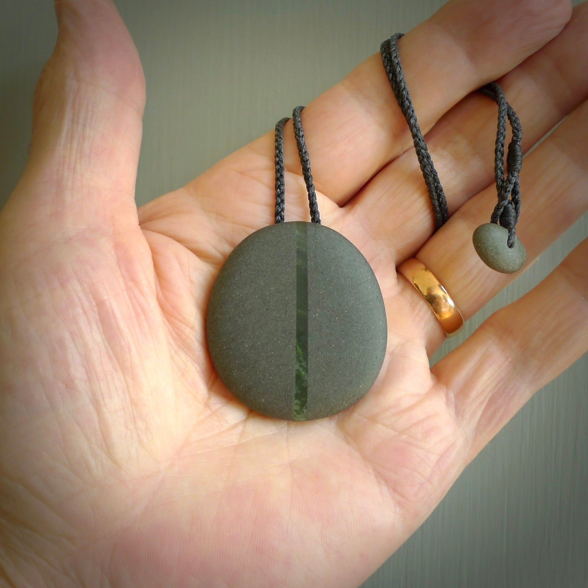 Greywacke stone pendant with New Zealand Jade Pounamu insert. Hand carved by Rhys Hall for NZ Pacific. Handmade jewellery for sale online. Delivered to you with express courier in one of our kete pouches.