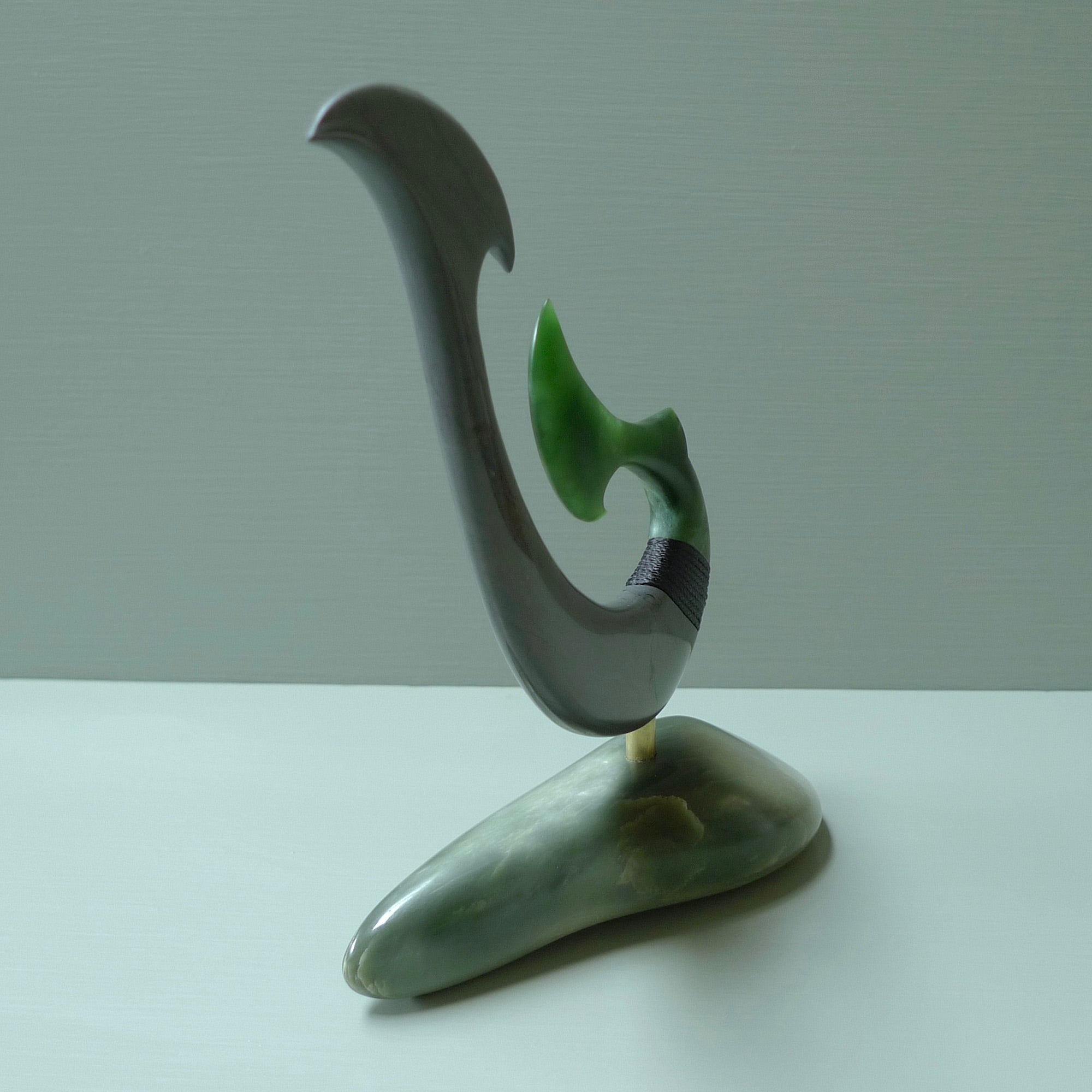 Hand carved large New Zealand Jade and Argillite Matau, hook carving displayed in a New Zealand Inanga Pounamu stand sculpture. Hand carved here in New Zealand by Kerry Thompson. This is a 'one only' sculpture, a beautiful display piece.