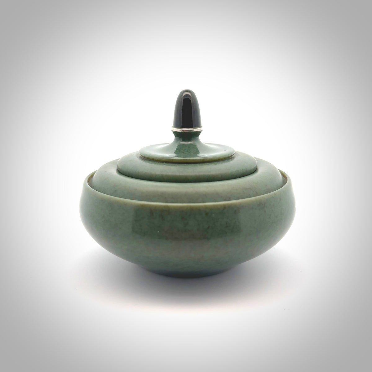 This photo shows a hand carved, Wyoming 'Sage' Nephrite Jade bowl sculpture. This 3.5 inch bowl carved from extremely fine-grained Sage. With Wyoming Black Jade and Sterling Silver, high domed centre grip. This hand crafted work of art was hand made by award winning New Zealand carver Donn Salt.