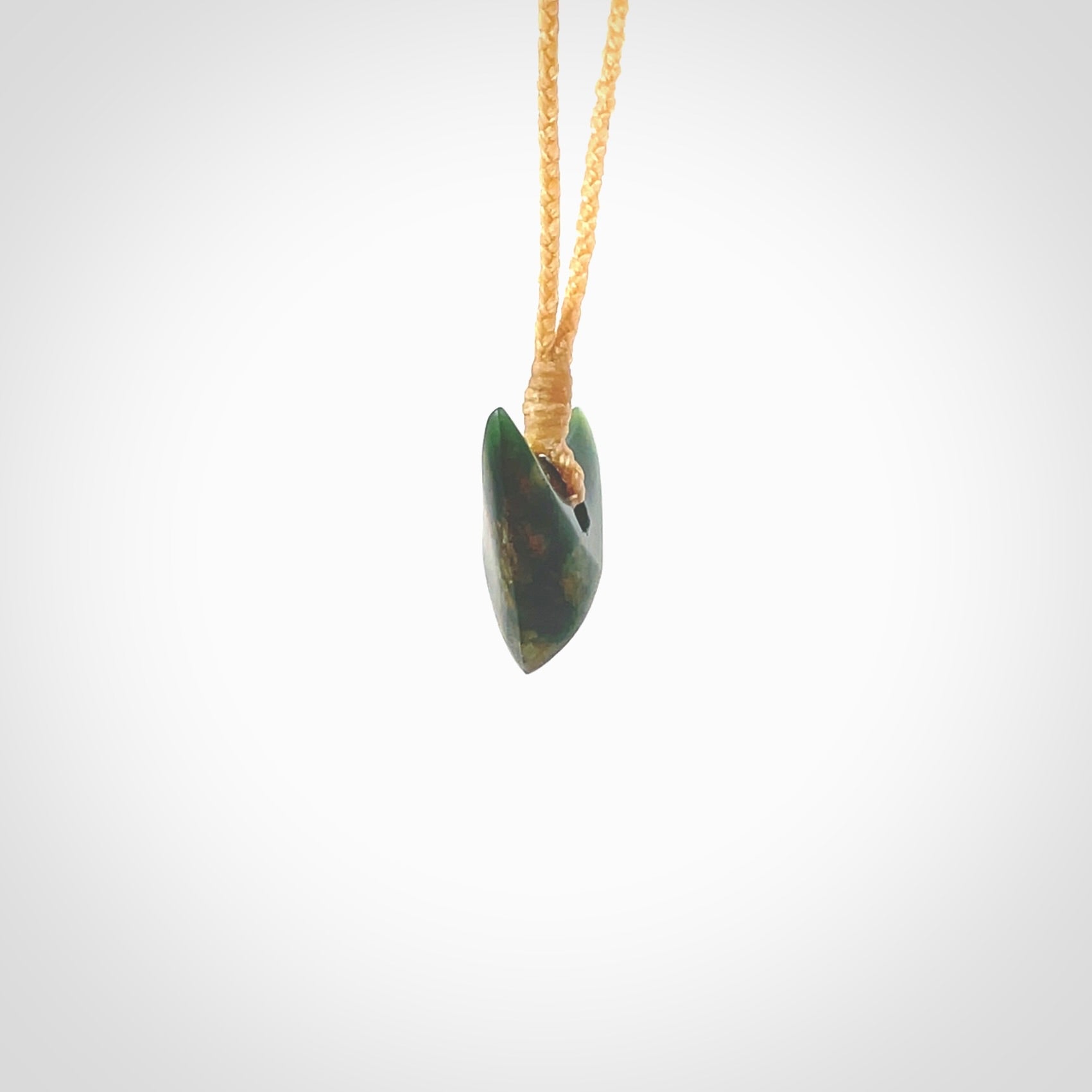 This is a lovely New Zealand Jade, pounamu drop pendant. Hand carved for us by Ric Moor. It is bound with an adjustable beige coloured cord which is length adjustable. Free worldwide shipping. The light reveals the internal structure and colour of the stone beautifully.