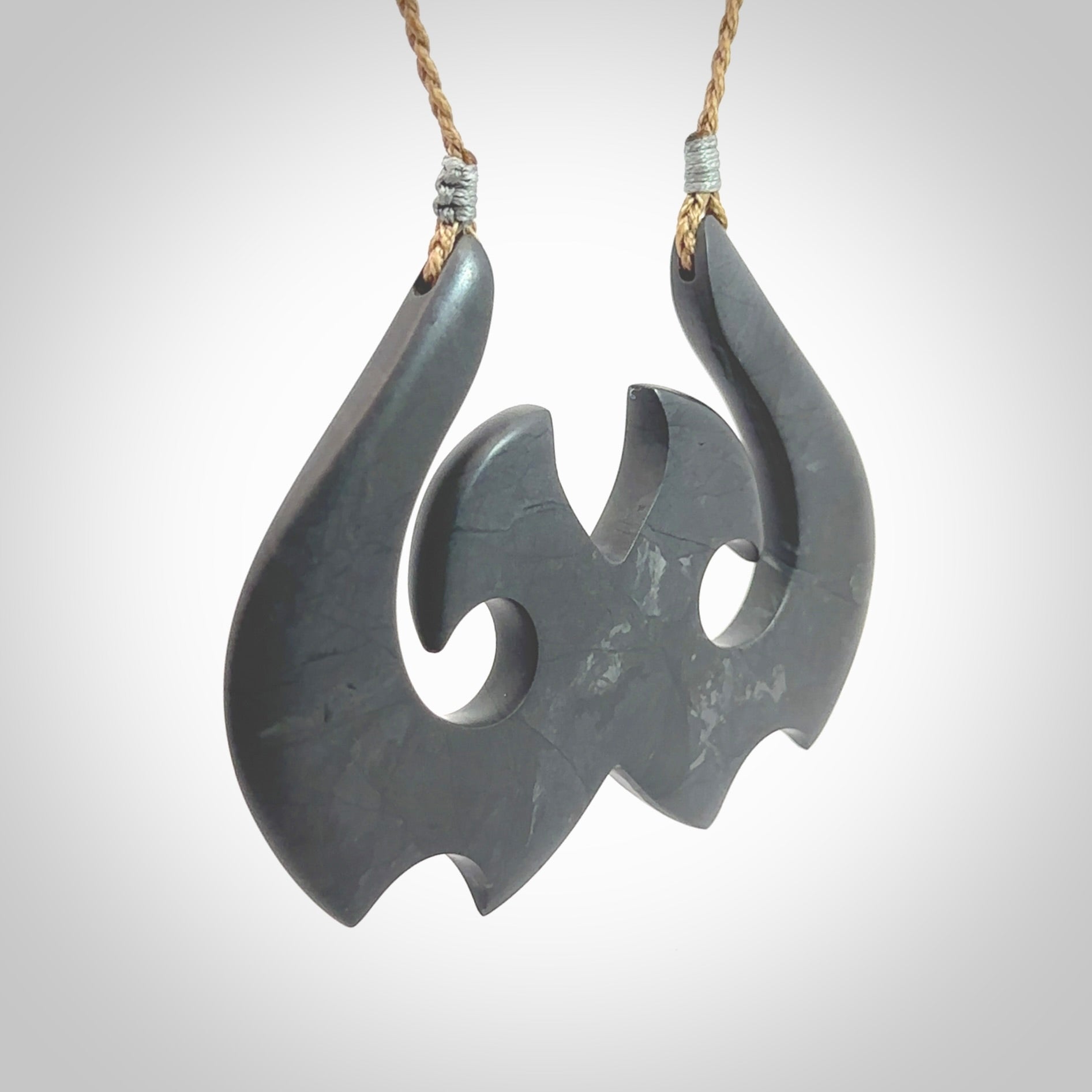 A hand carved large New Zealand Argillite double Hook, Matau, necklace. The cord is a kalahari tan colour and is adjustable in length. A large sized hand made double hook necklace by New Zealand artist Rueben Tipene. One off work of art to wear.