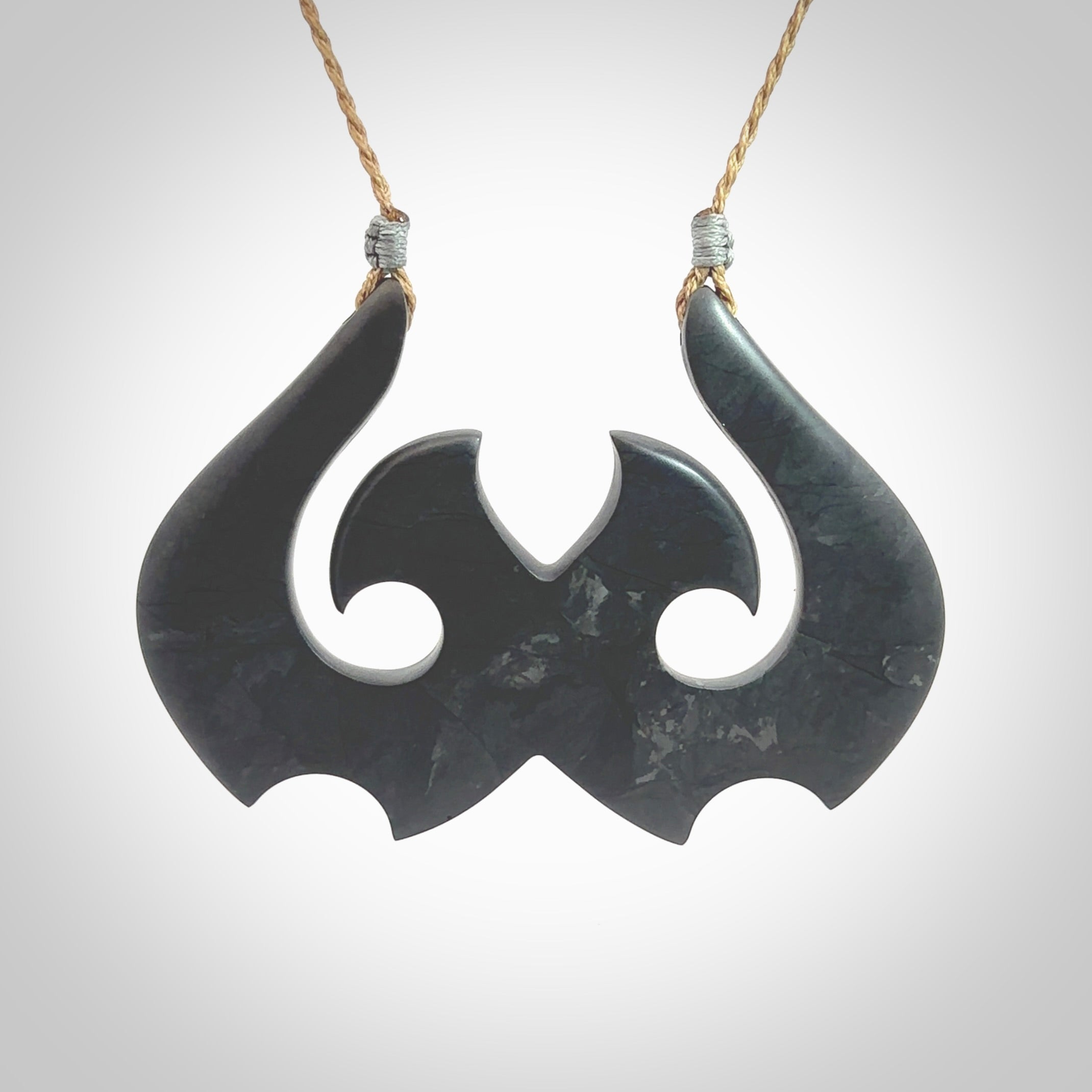 A hand carved large New Zealand Argillite double Hook, Matau, necklace. The cord is a kalahari tan colour and is adjustable in length. A large sized hand made double hook necklace by New Zealand artist Rueben Tipene. One off work of art to wear.