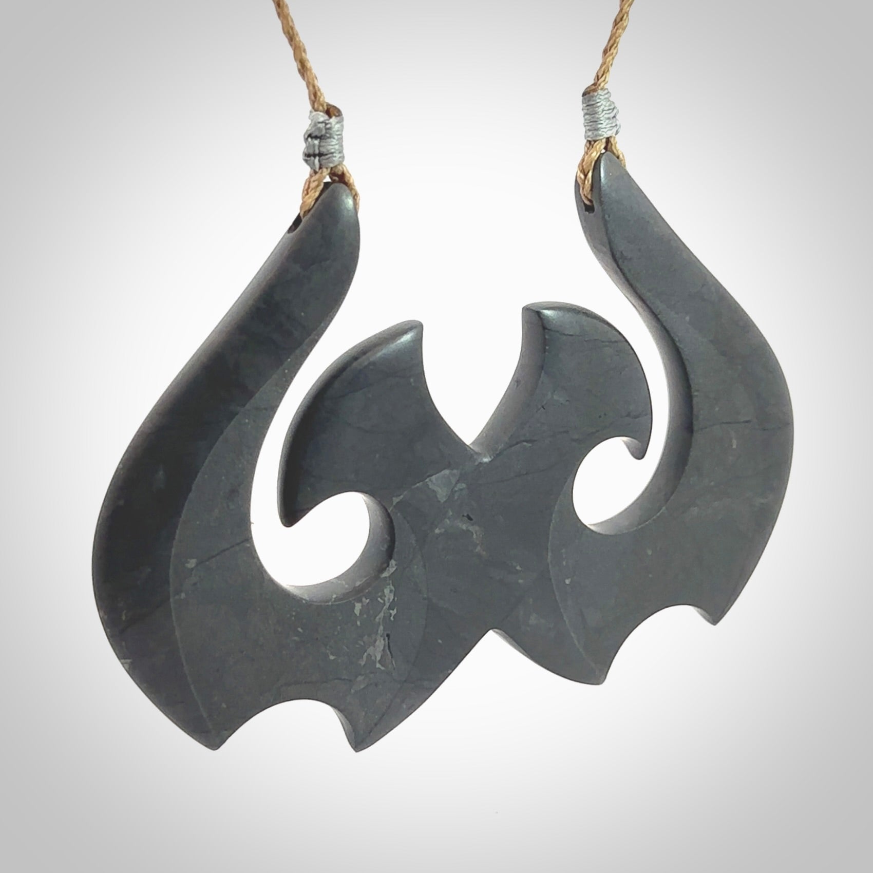 A hand carved large New Zealand Argillite double Hook, Matau, necklace. The cord is a kalahari tan colour and is adjustable in length. A large sized hand made double hook necklace by New Zealand artist Rueben Tipene. One off work of art to wear.