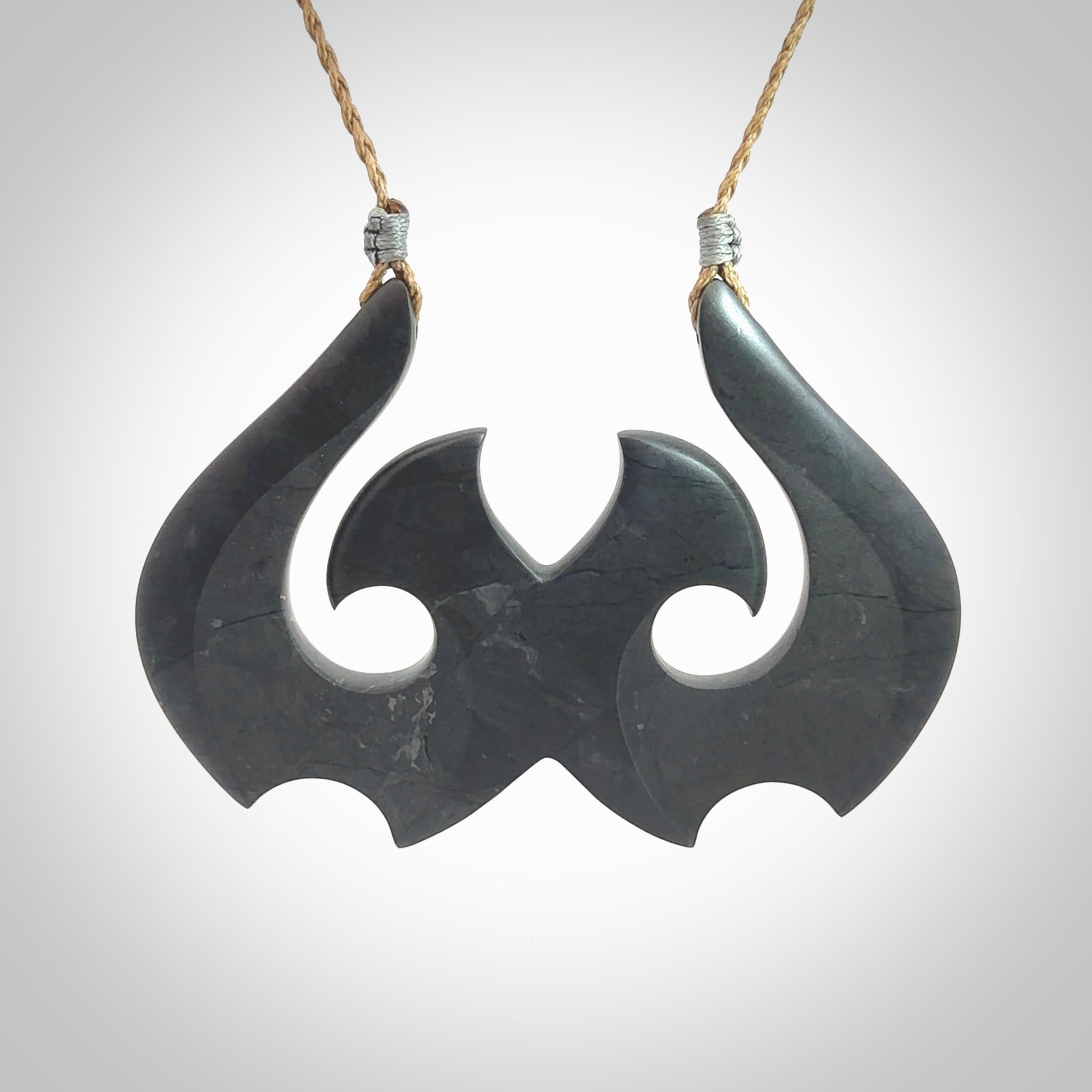 A hand carved large New Zealand Argillite double Hook, Matau, necklace. The cord is a kalahari tan colour and is adjustable in length. A large sized hand made double hook necklace by New Zealand artist Rueben Tipene. One off work of art to wear.