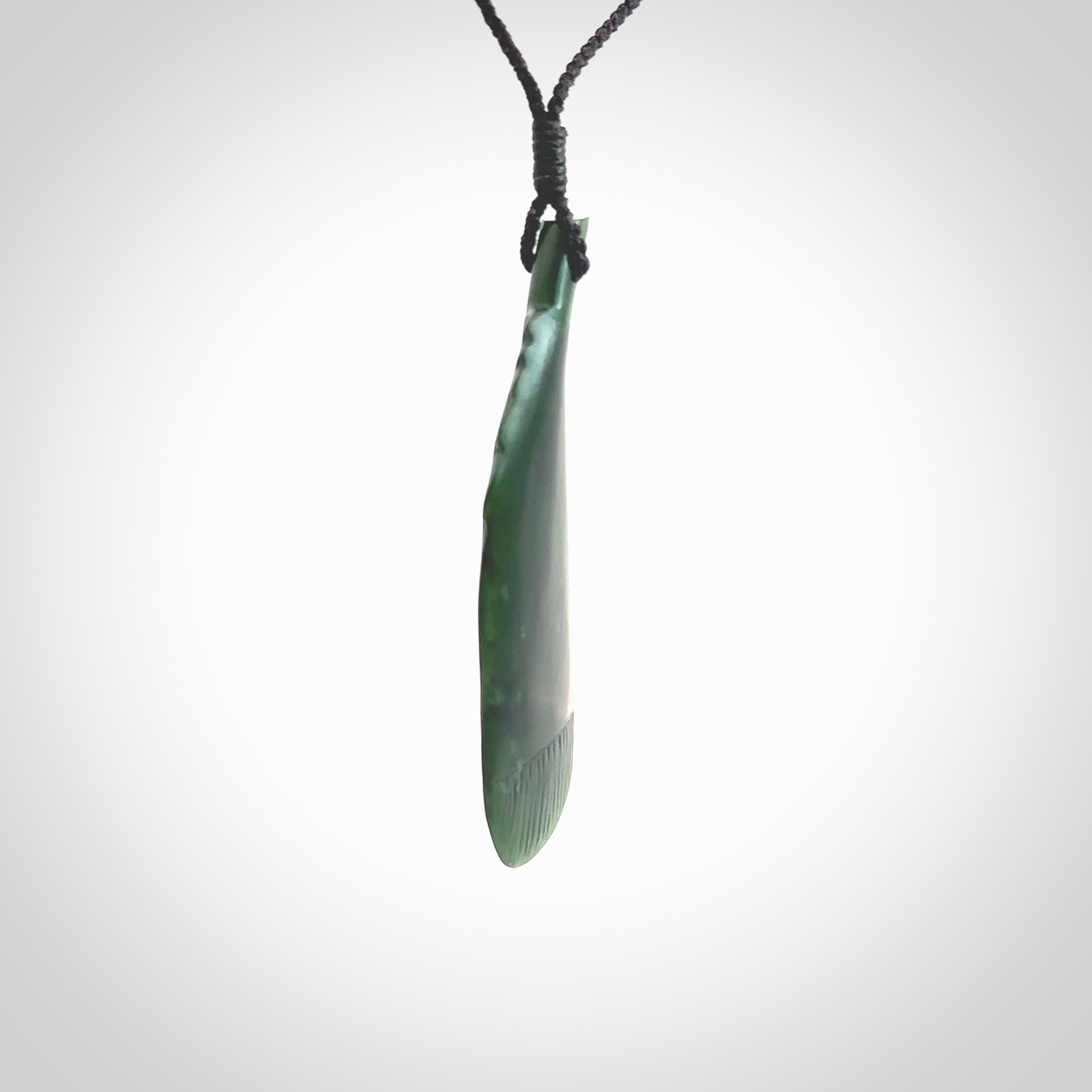 Hand carved New Zealand Jade huia feather pendant. Made by Ana Krakosky for NZ Pacific in New Zealand Pounamu, jade. A beautiful dark green jade huia feather drop necklace with black adjustable cord.