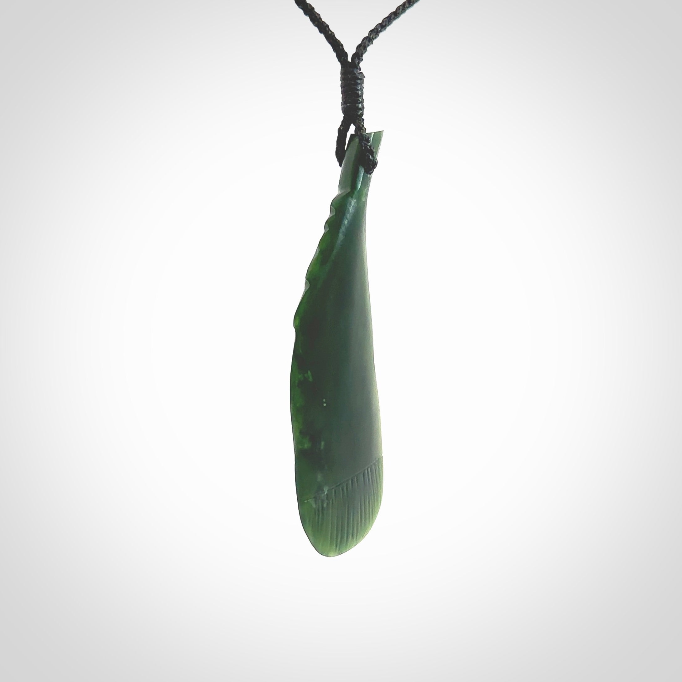 Hand carved New Zealand Jade huia feather pendant. Made by Ana Krakosky for NZ Pacific in New Zealand Pounamu, jade. A beautiful dark green jade huia feather drop necklace with black adjustable cord.