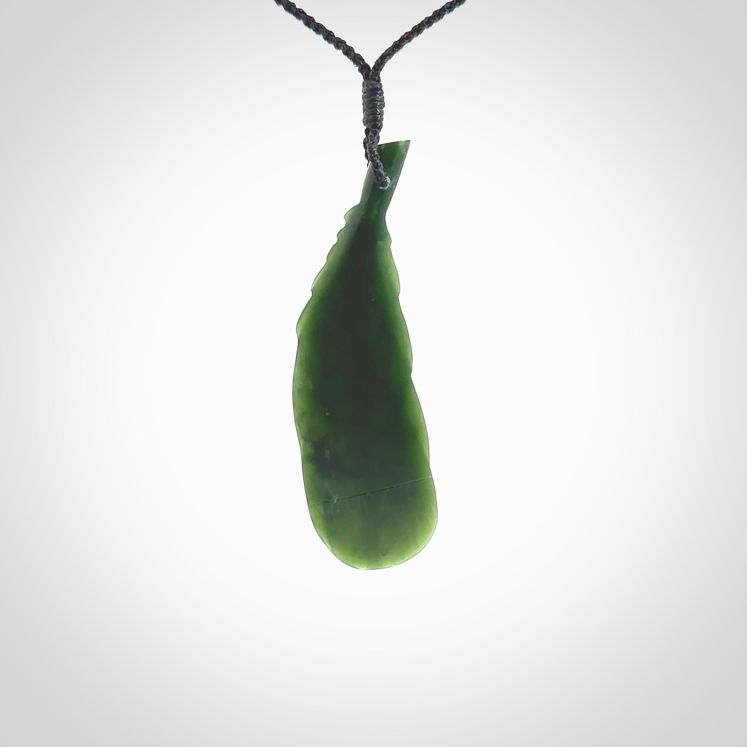 Hand carved New Zealand Jade huia feather pendant. Made by Ana Krakosky for NZ Pacific in New Zealand Pounamu, jade. A beautiful dark green jade huia feather drop necklace with black adjustable cord.