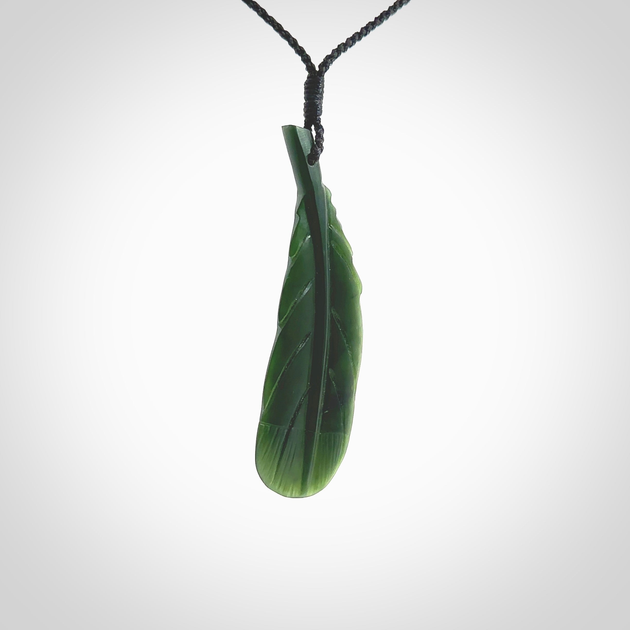 Hand carved New Zealand Jade huia feather pendant. Made by Ana Krakosky for NZ Pacific in New Zealand Pounamu, jade. A beautiful dark green jade huia feather drop necklace with black adjustable cord.