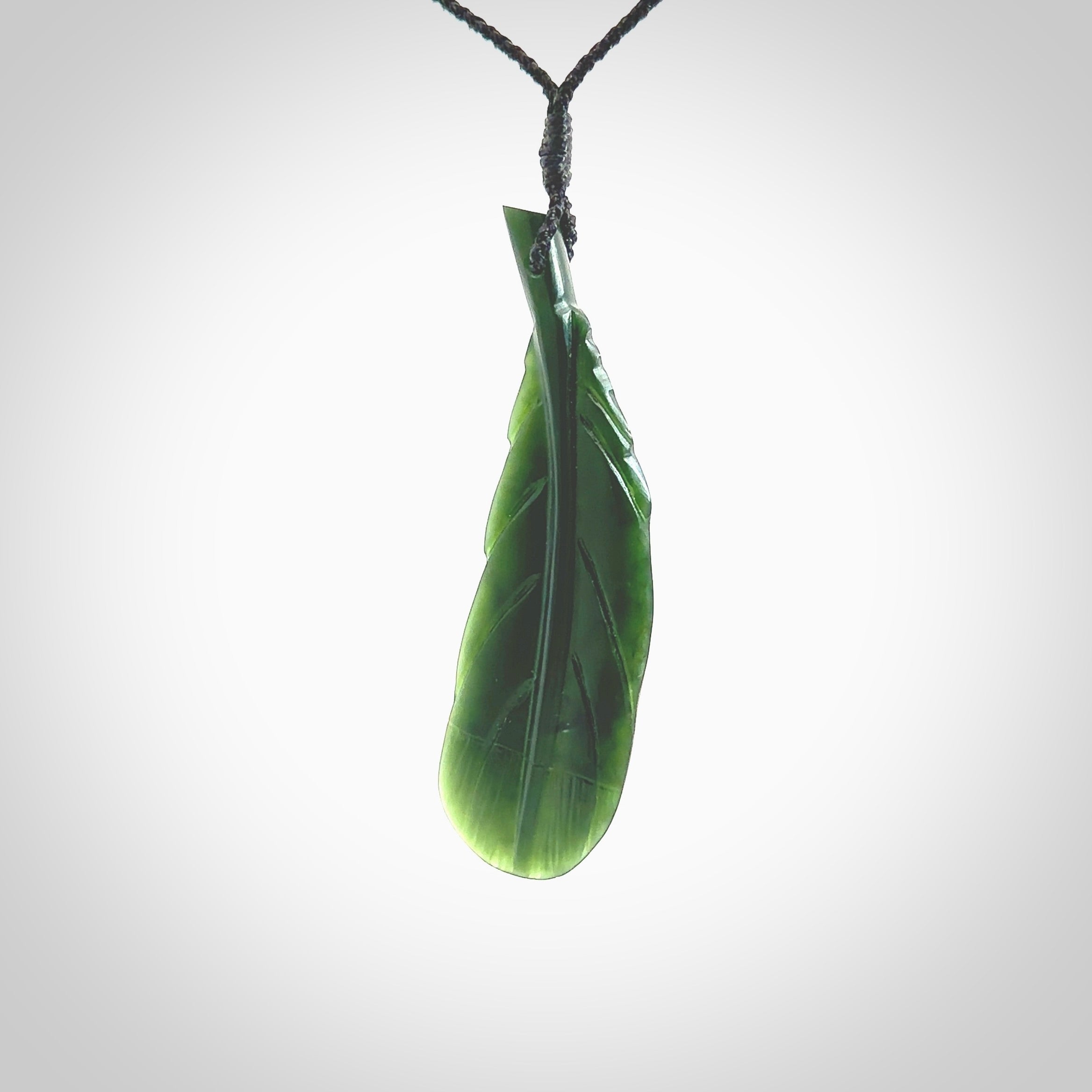 Hand carved New Zealand Jade huia feather pendant. Made by Ana Krakosky for NZ Pacific in New Zealand Pounamu, jade. A beautiful dark green jade huia feather drop necklace with black adjustable cord.