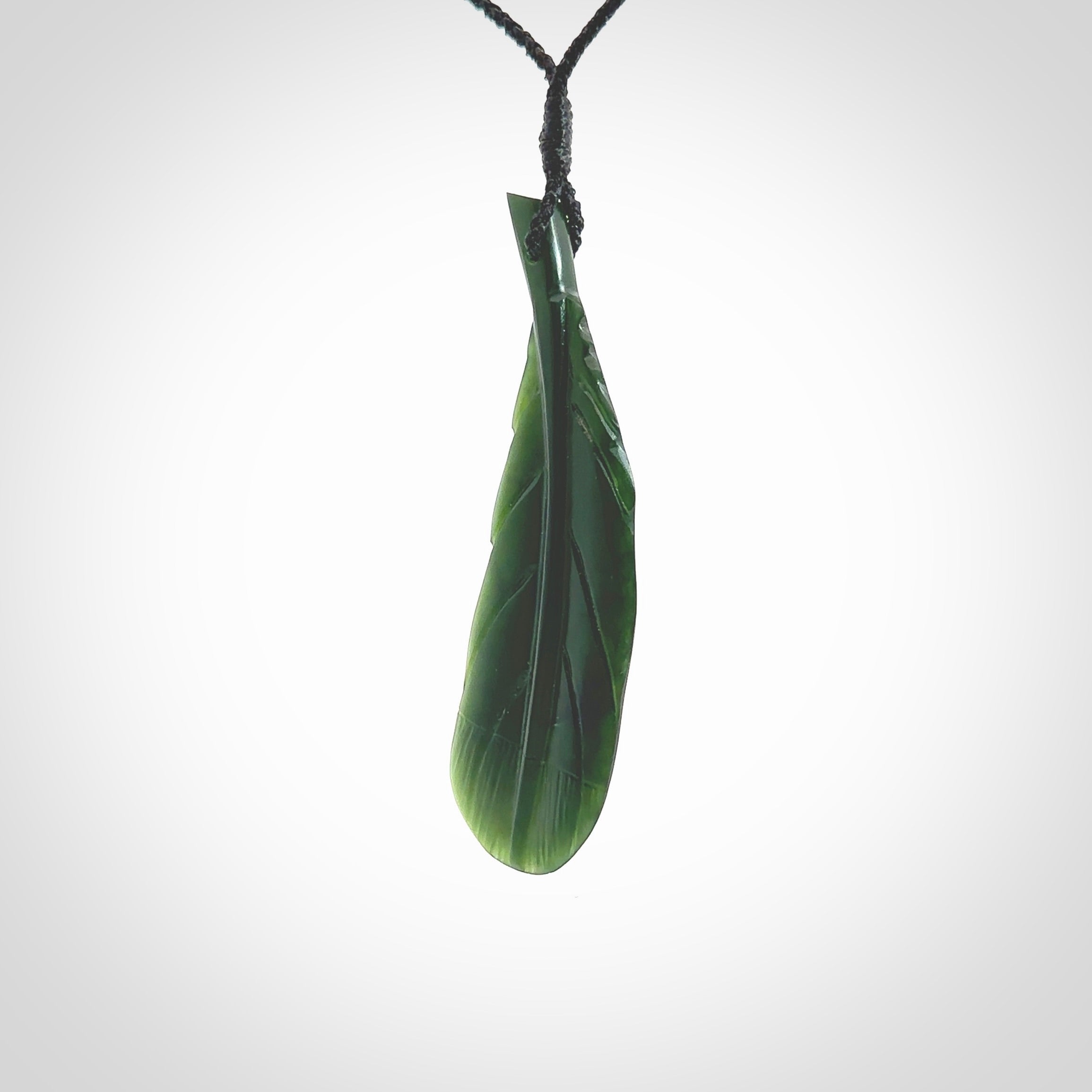 Hand carved New Zealand Jade huia feather pendant. Made by Ana Krakosky for NZ Pacific in New Zealand Pounamu, jade. A beautiful dark green jade huia feather drop necklace with black adjustable cord.