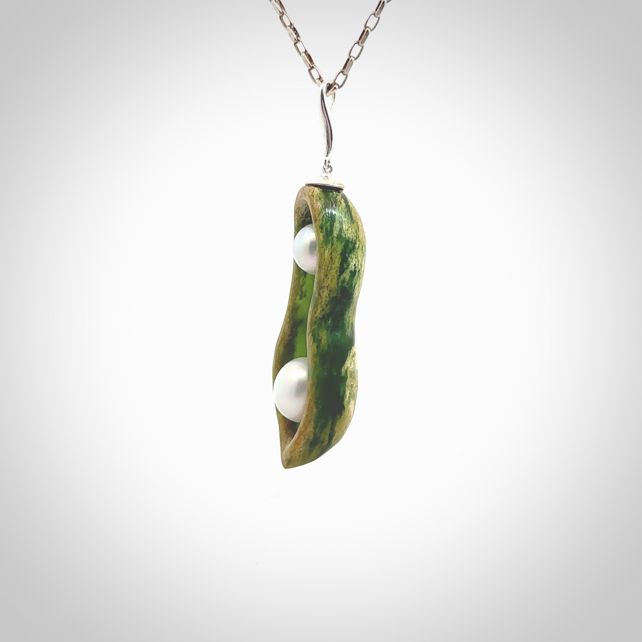 Hand carved New Zealand Marsden Jade two peas in a pod drop pendant with two pearl inlays. Made by Ana Krakosky for NZ Pacific in New Zealand Pounamu, flower jade with real pearls. A beautiful dark green and orange jade representing two peas in a pod. A drop with pearl inserts necklace with long sterling silver chain. One only, provided in a wooden gift box and delivered with express courier.