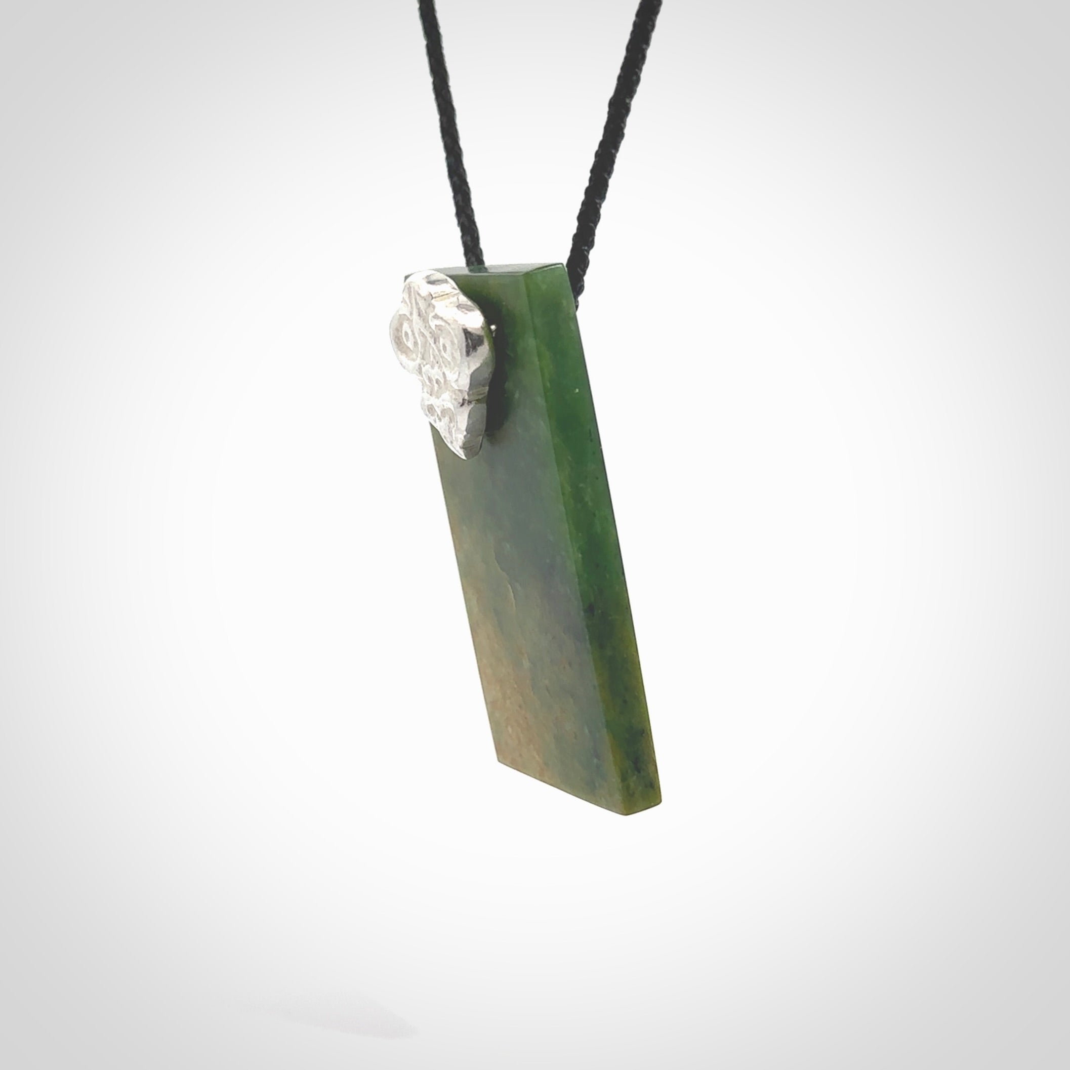 Hand carved New Zealand flower Jade rectangle drop with sterling silver tiki face pendant. Made by Ana Krakosky for NZ Pacific in New Zealand Pounamu, jade. A beautiful orange and green marsden flower jade medium sized rectangle drop necklace with silver cast tiki face, provided on a black adjustable cord.