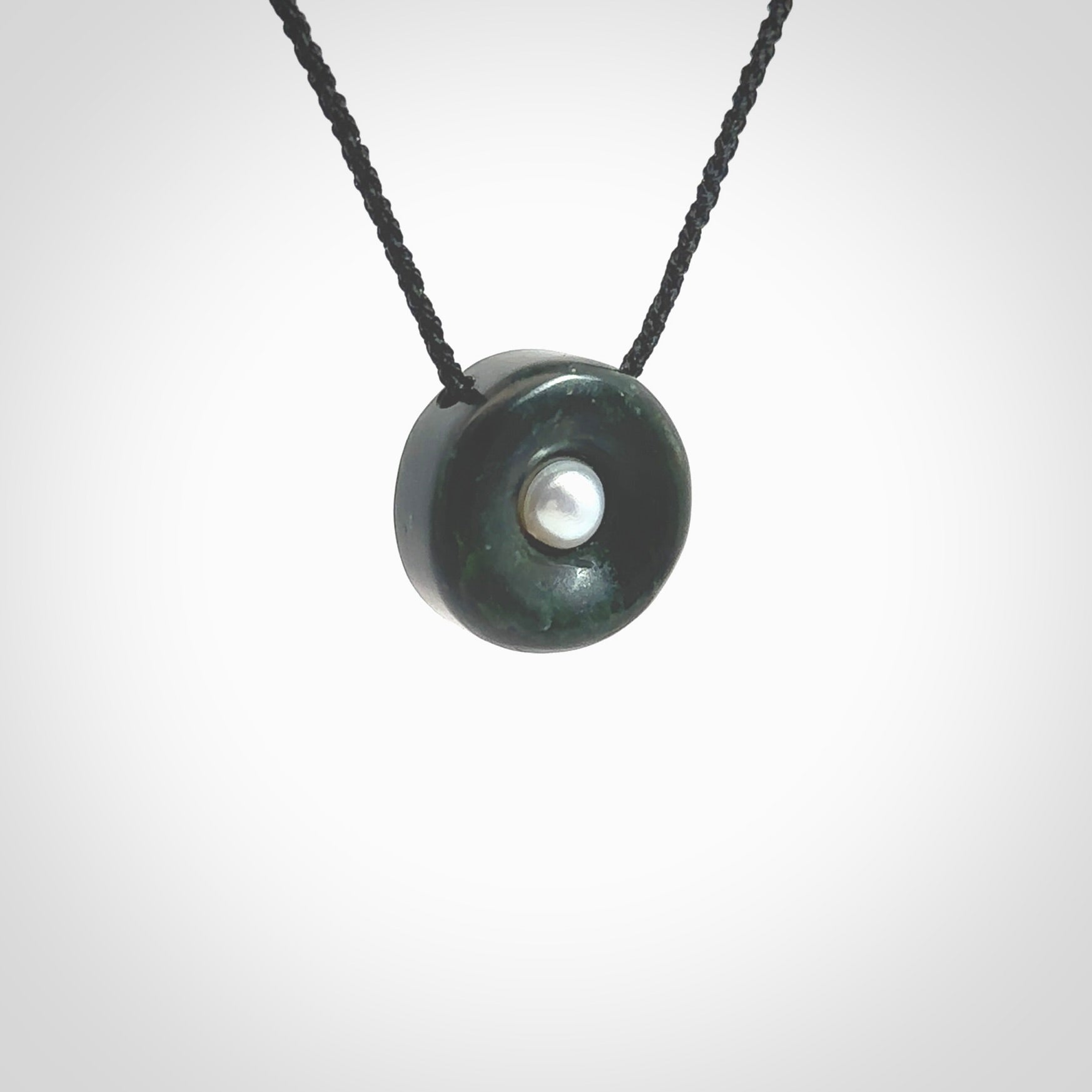 Hand carved New Zealand Jade donut drop pendant with pearl centre. Made by Ana Krakosky for NZ Pacific in New Zealand Pounamu, jade with real pearl heart. A beautiful dark green jade circle drop with pearl insert necklace with black adjustable cord.