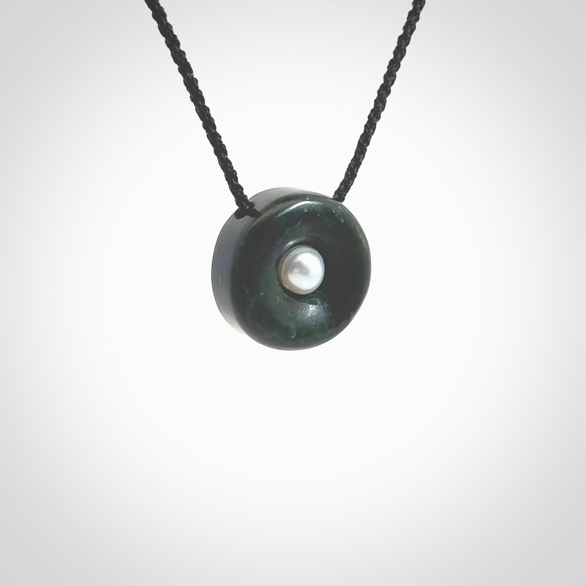 Hand carved New Zealand Jade donut drop pendant with pearl centre. Made by Ana Krakosky for NZ Pacific in New Zealand Pounamu, jade with real pearl heart. A beautiful dark green jade circle drop with pearl insert necklace with black adjustable cord.