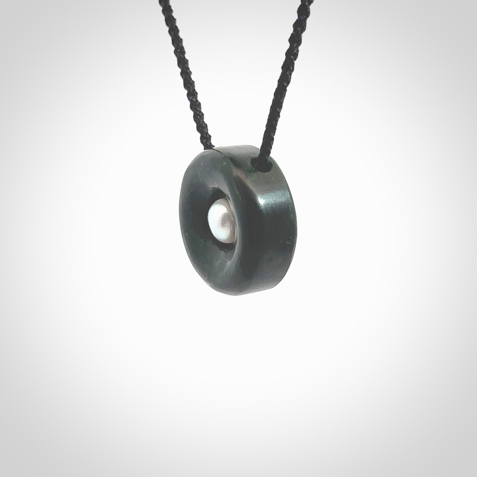 Hand carved New Zealand Jade donut drop pendant with pearl centre. Made by Ana Krakosky for NZ Pacific in New Zealand Pounamu, jade with real pearl heart. A beautiful dark green jade circle drop with pearl insert necklace with black adjustable cord.