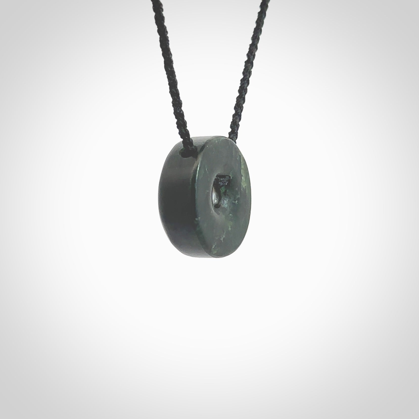 Hand carved New Zealand Jade donut drop pendant with pearl centre. Made by Ana Krakosky for NZ Pacific in New Zealand Pounamu, jade with real pearl heart. A beautiful dark green jade circle drop with pearl insert necklace with black adjustable cord.