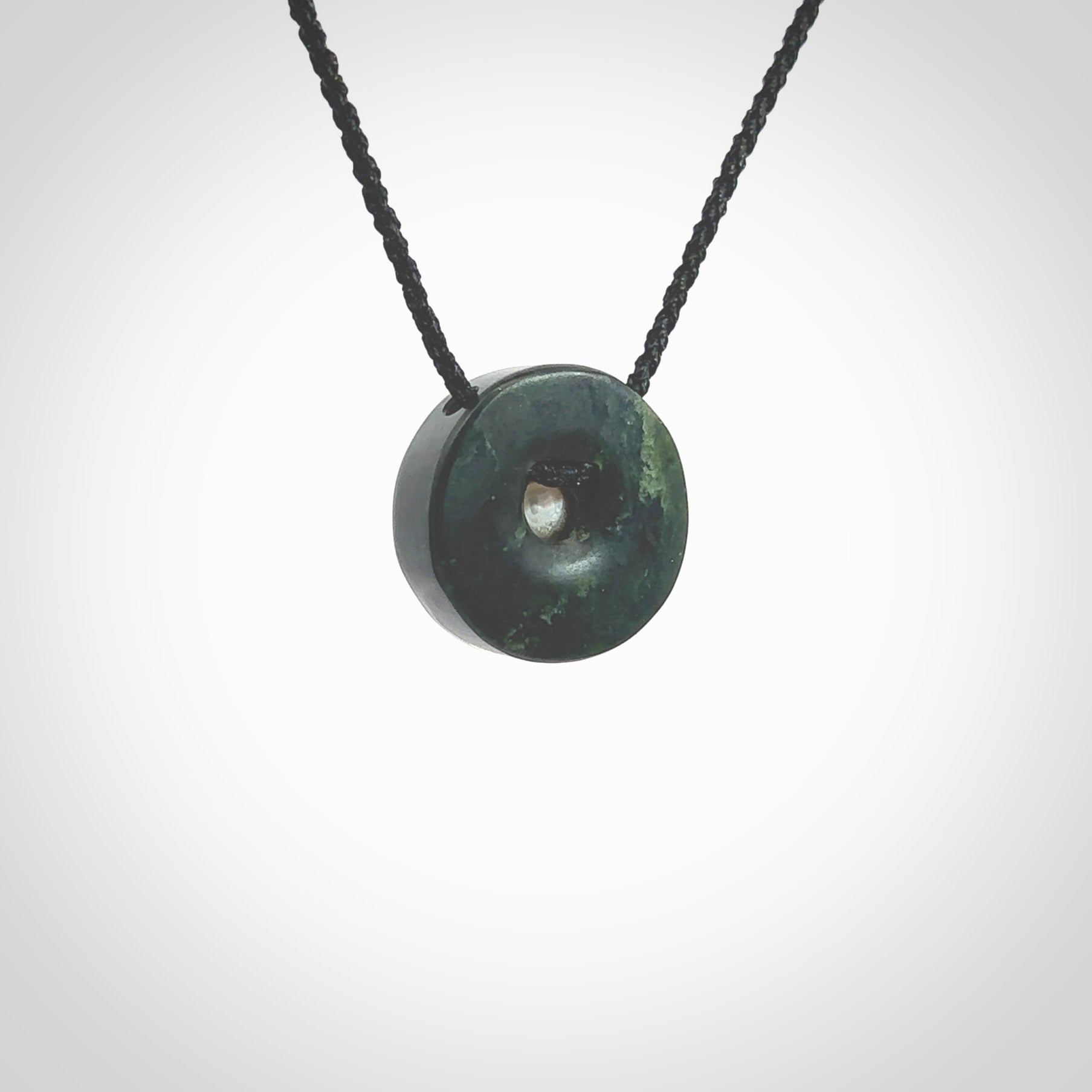 Hand carved New Zealand Jade donut drop pendant with pearl centre. Made by Ana Krakosky for NZ Pacific in New Zealand Pounamu, jade with real pearl heart. A beautiful dark green jade circle drop with pearl insert necklace with black adjustable cord.