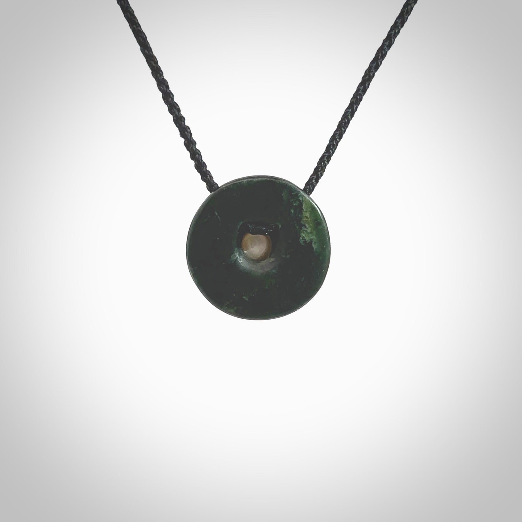 Hand carved New Zealand Jade donut drop pendant with pearl centre. Made by Ana Krakosky for NZ Pacific in New Zealand Pounamu, jade with real pearl heart. A beautiful dark green jade circle drop with pearl insert necklace with black adjustable cord.