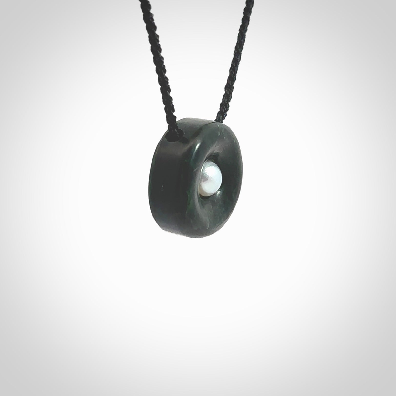 Hand carved New Zealand Jade donut drop pendant with pearl centre. Made by Ana Krakosky for NZ Pacific in New Zealand Pounamu, jade with real pearl heart. A beautiful dark green jade circle drop with pearl insert necklace with black adjustable cord.