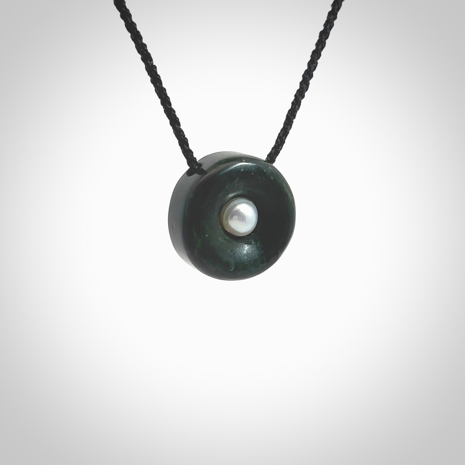 Hand carved New Zealand Jade donut drop pendant with pearl centre. Made by Ana Krakosky for NZ Pacific in New Zealand Pounamu, jade with real pearl heart. A beautiful dark green jade circle drop with pearl insert necklace with black adjustable cord.