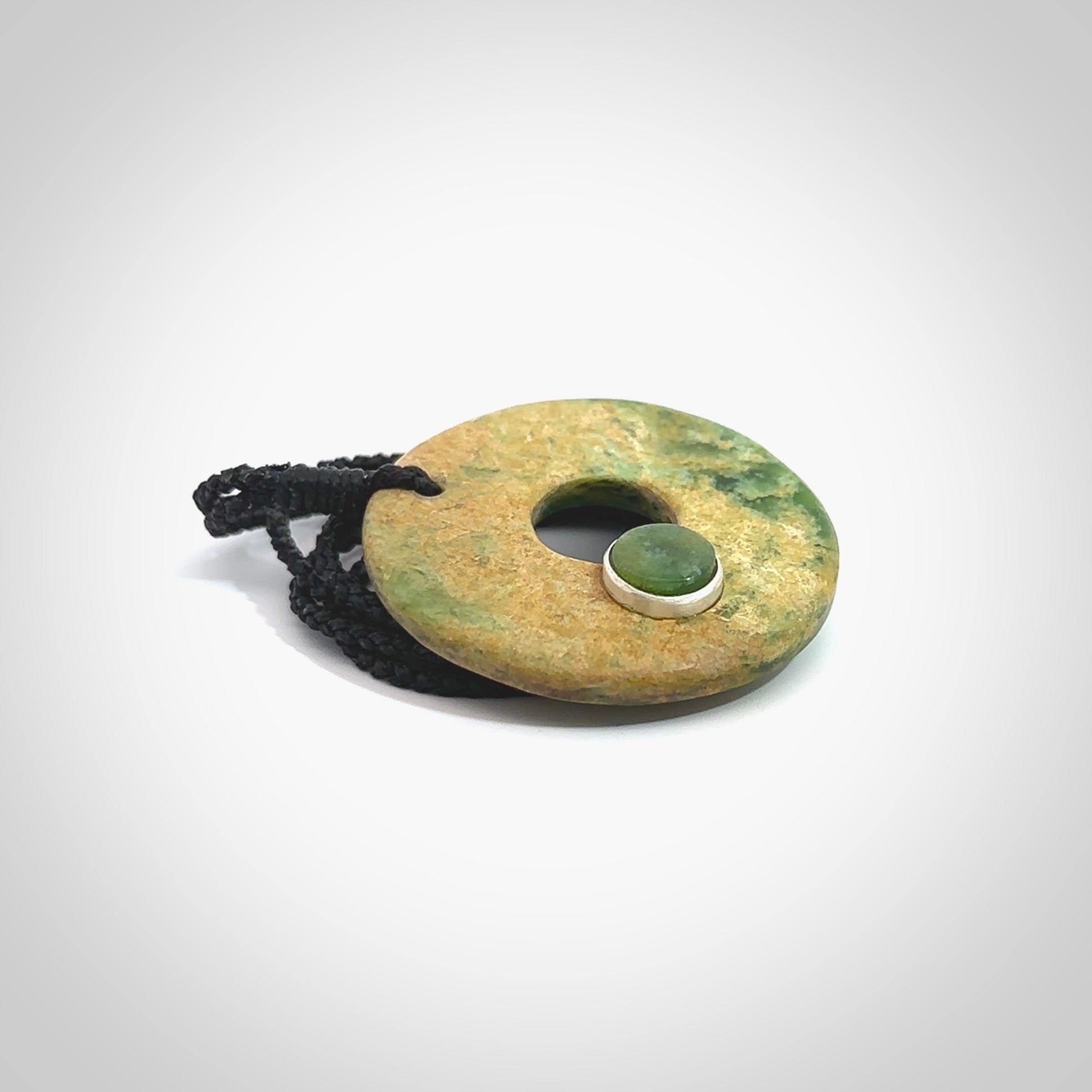 Hand carved New Zealand flower Jade disc drop pendant with smaller pounamu and silver insert. Made by Ana Krakosky for NZ Pacific in New Zealand Pounamu, jade. A beautiful orange and green jade disc necklace with black adjustable cord.