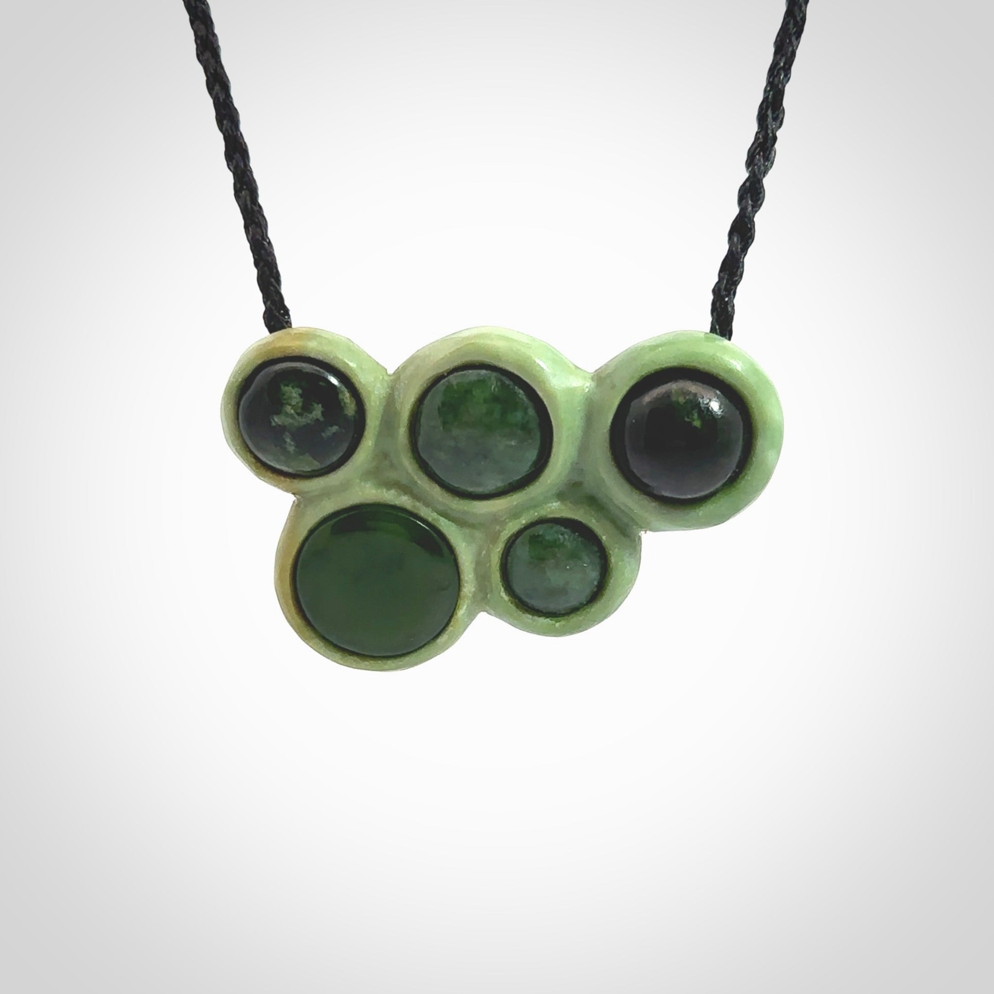 Hand carved New Zealand Jade bubbles drop pendant. Made by Ana Krakosky for NZ Pacific in New Zealand Pounamu, jade. A beautiful light and dark green jade drop of bubbles necklace with black adjustable cord.