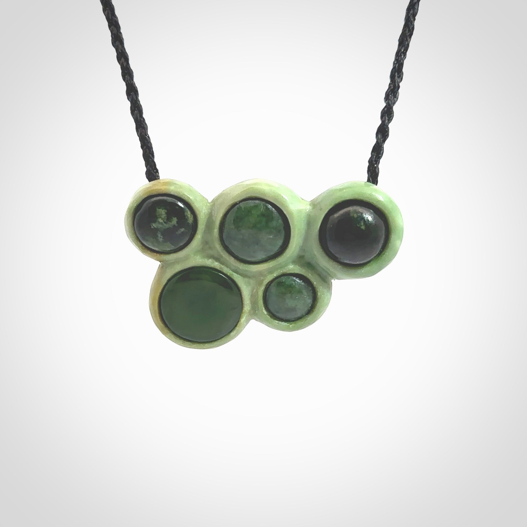 Hand carved New Zealand Jade bubbles drop pendant. Made by Ana Krakosky for NZ Pacific in New Zealand Pounamu, jade. A beautiful light and dark green jade drop of bubbles necklace with black adjustable cord.