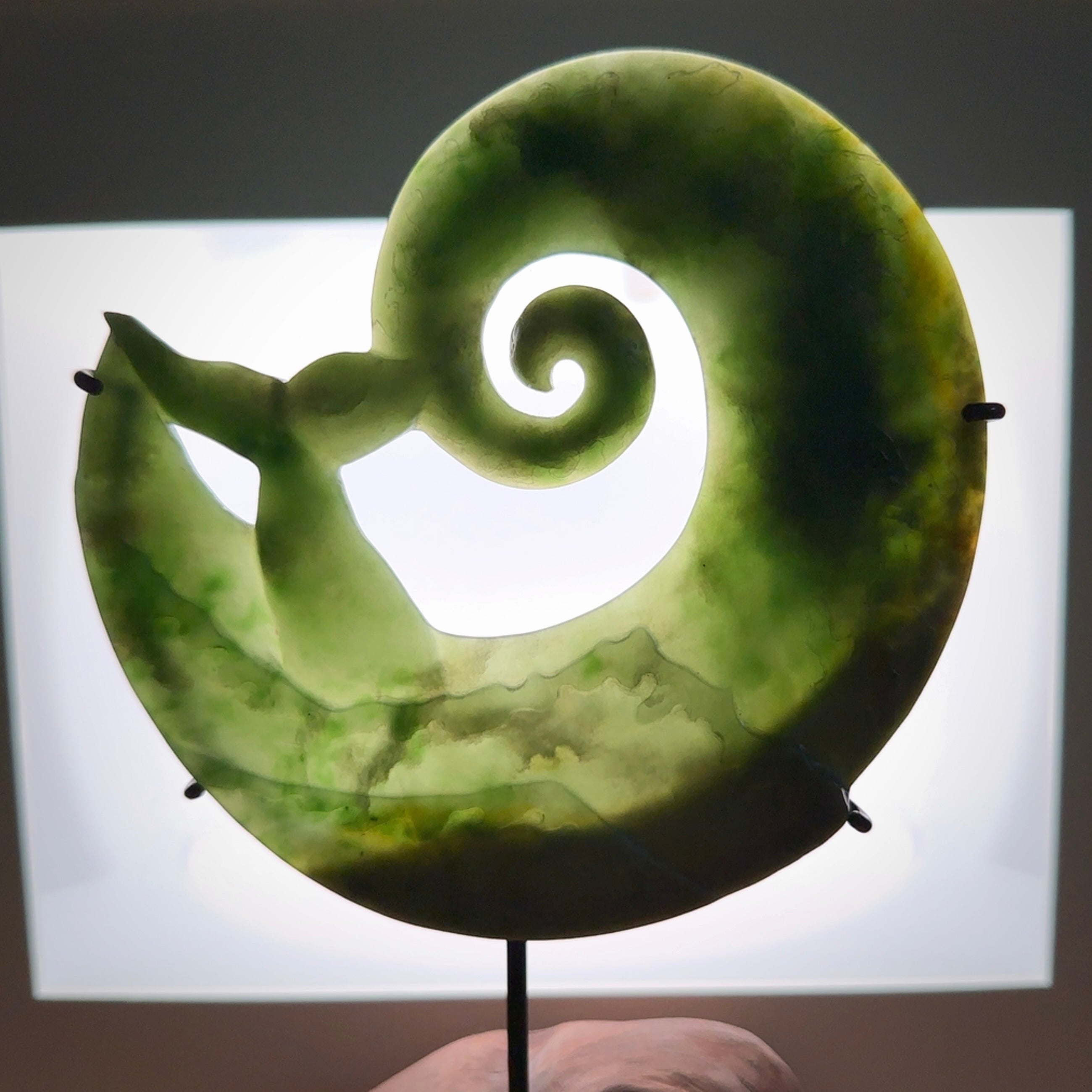 A photo of a New Zealand Jade whale tail in a wave sculpture with Rata Burr stand. This is a statement piece - hand crafted here in New Zealand by Ana Krakosky. Unique Art to display. Gifts for all lovers of hand made sculptures.