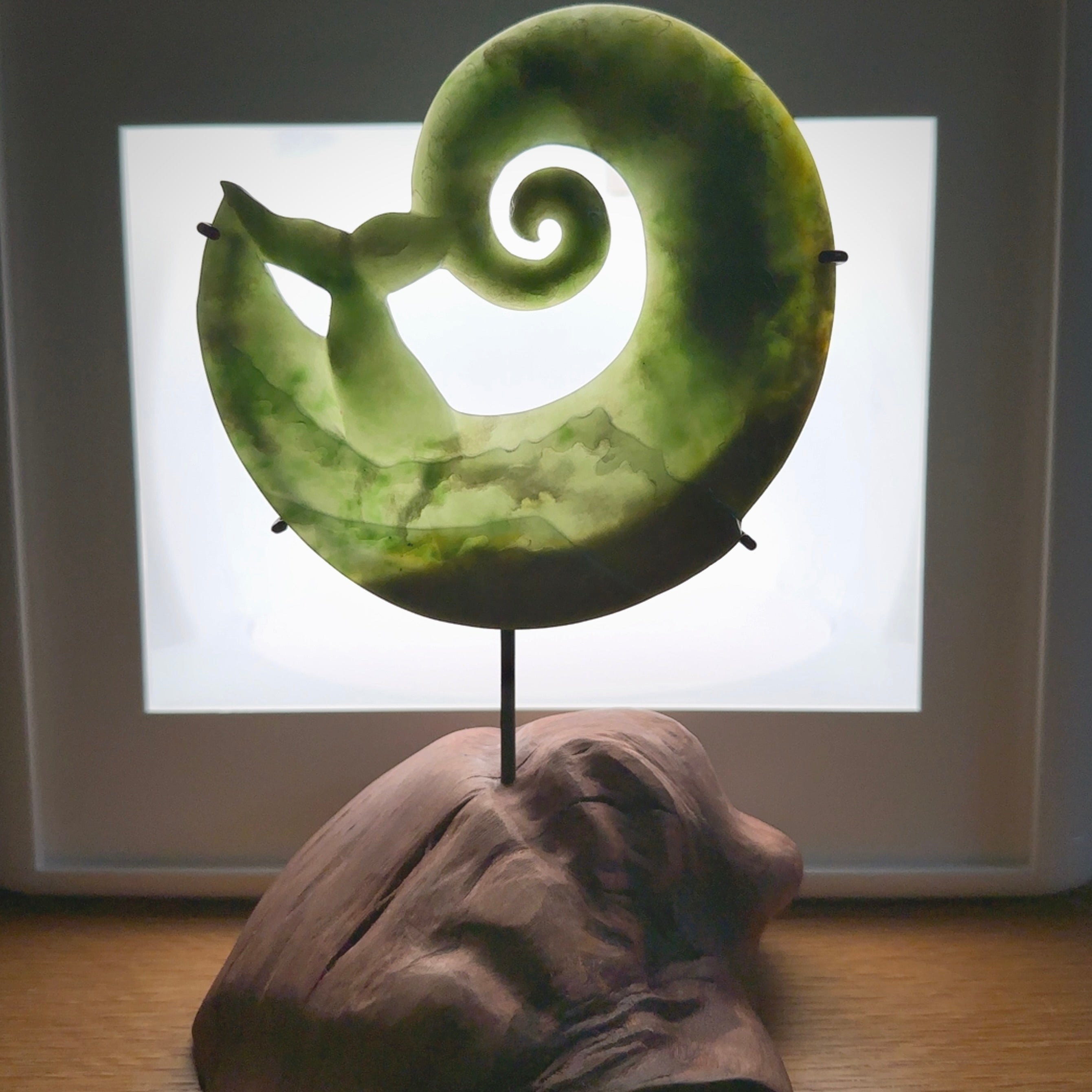 A photo of a New Zealand Jade whale tail in a wave sculpture with Rata Burr stand. This is a statement piece - hand crafted here in New Zealand by Ana Krakosky. Unique Art to display. Gifts for all lovers of hand made sculptures.