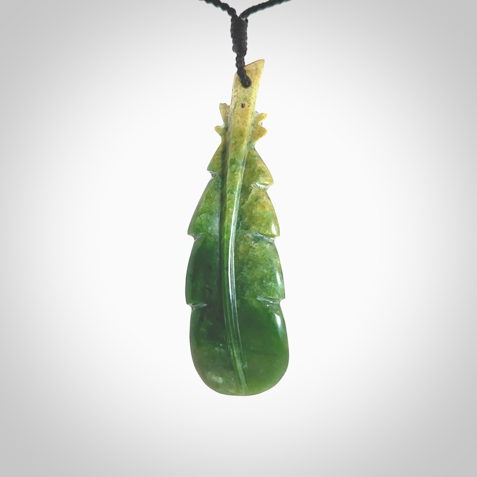 Hand carved New Zealand Marsden Jade feather pendant. Made by Ana Krakosky for NZ Pacific in New Zealand Pounamu, jade. A beautiful dark green and orange jade feather drop necklace with black adjustable cord.