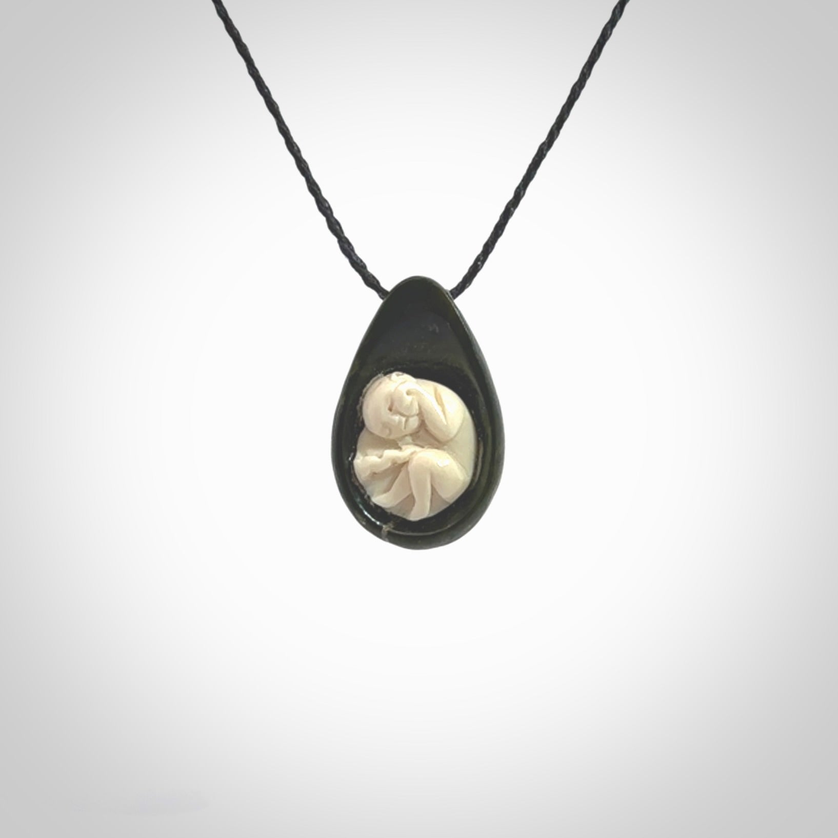 A hand carved baby in the womb pendant made from a jade and bone. This is a work of art carved in jade and bone. We deliver this pendant to you on a plaited cord. Delivery with Express Courier is included in the price.