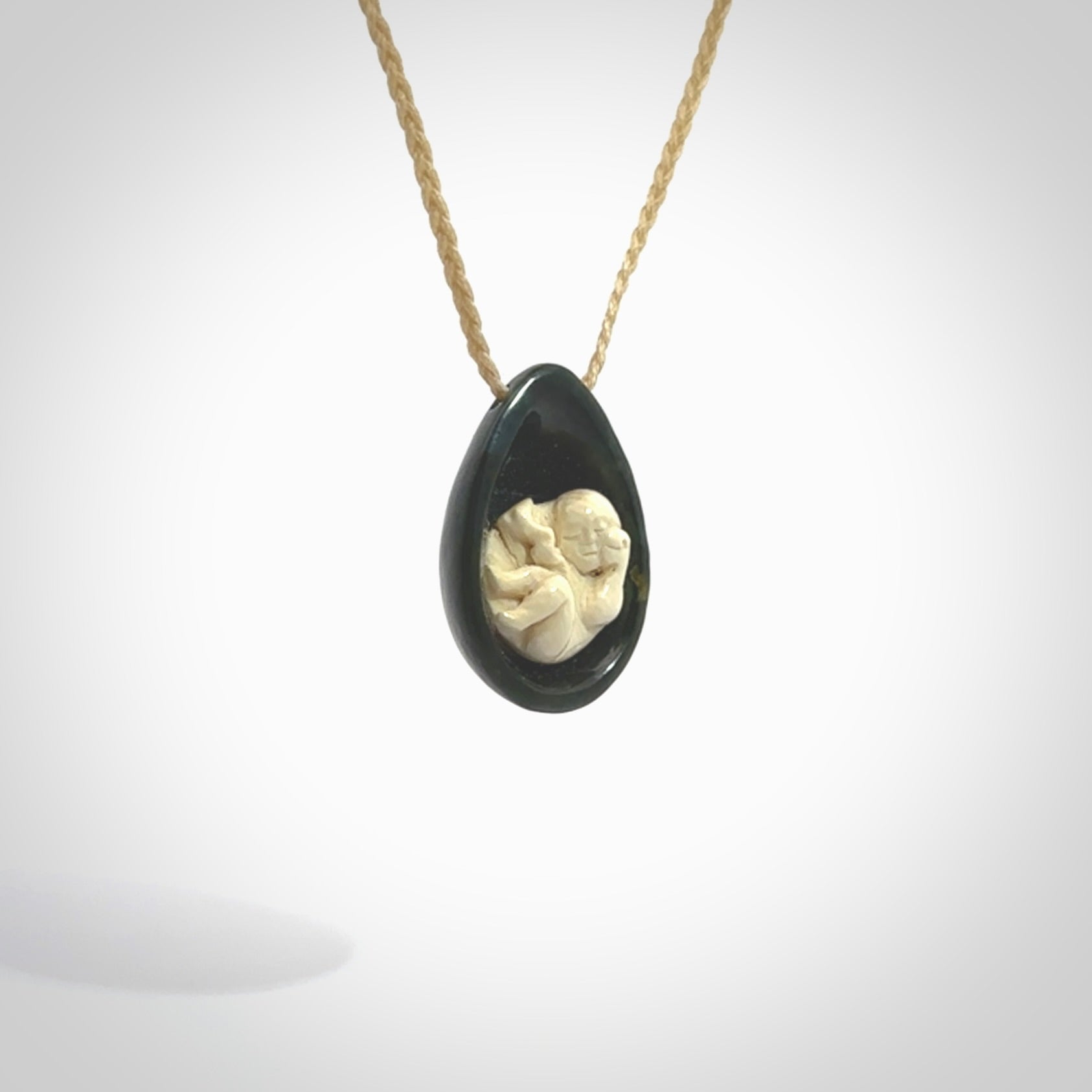 A hand carved baby in the womb pendant made from a jade and bone. This is a work of art carved in jade and bone. We deliver this pendant to you on a plaited cord. Delivery with Express Courier is included in the price.